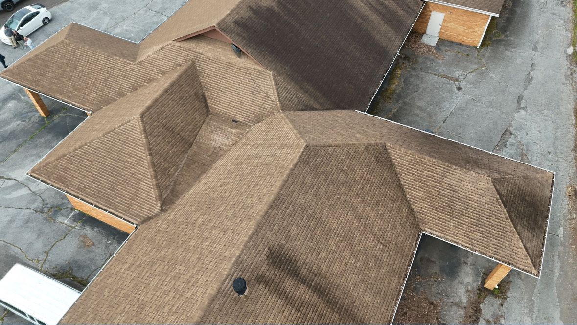 Brown shingled roof of a building with multiple sections against an asphalt background.