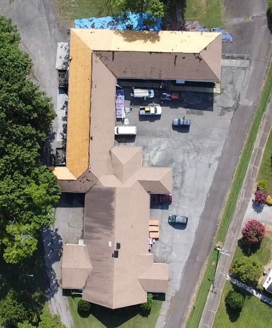 Overhead view of a building with brown roof partially under construction, vehicles in parking area.