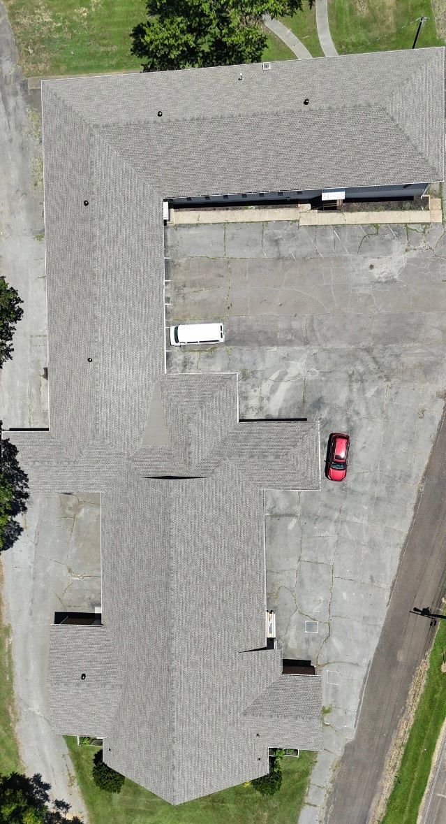 Aerial view of a building with a gray roof, parking lot, and a red car.