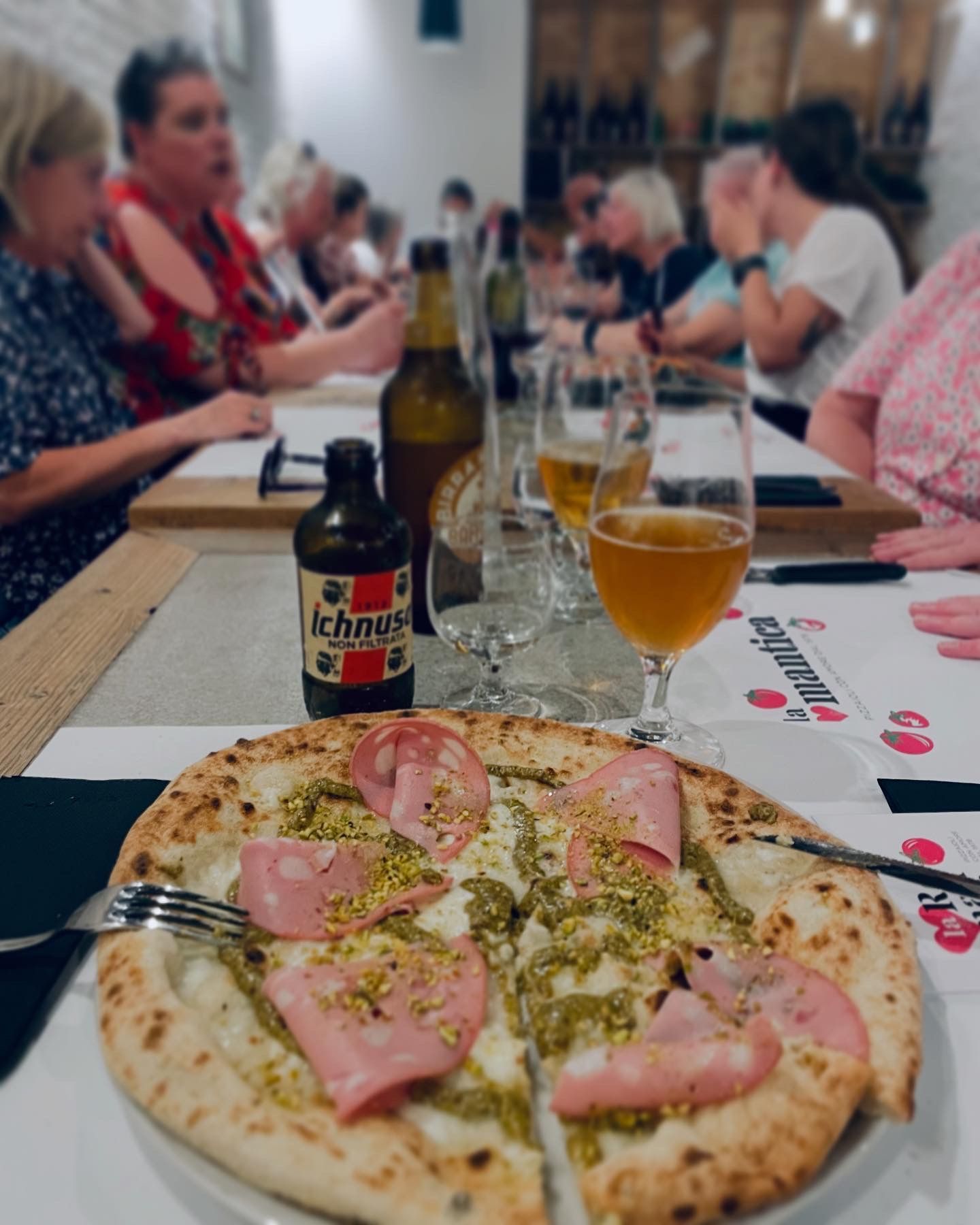 Pizza with beer and a group of people at a restaurant table.