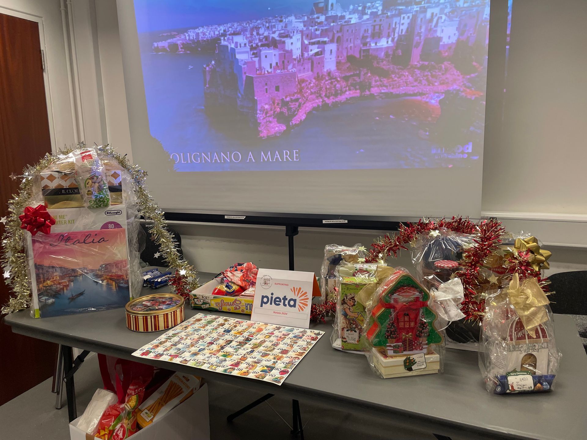 A table with gift baskets, and a projected image of a coastal town; festive setting.