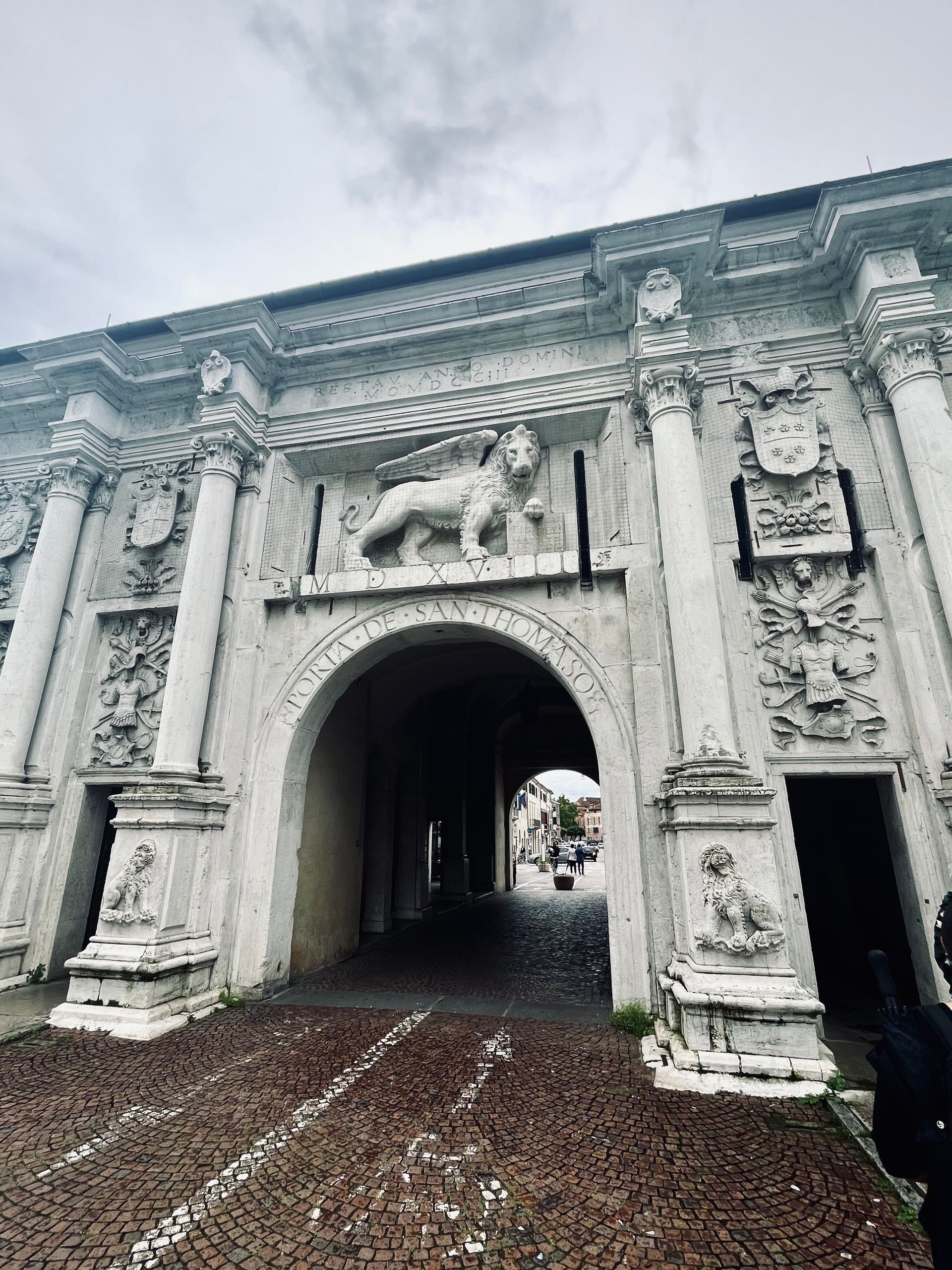 White arched stone gate with a lion statue and decorative carvings.