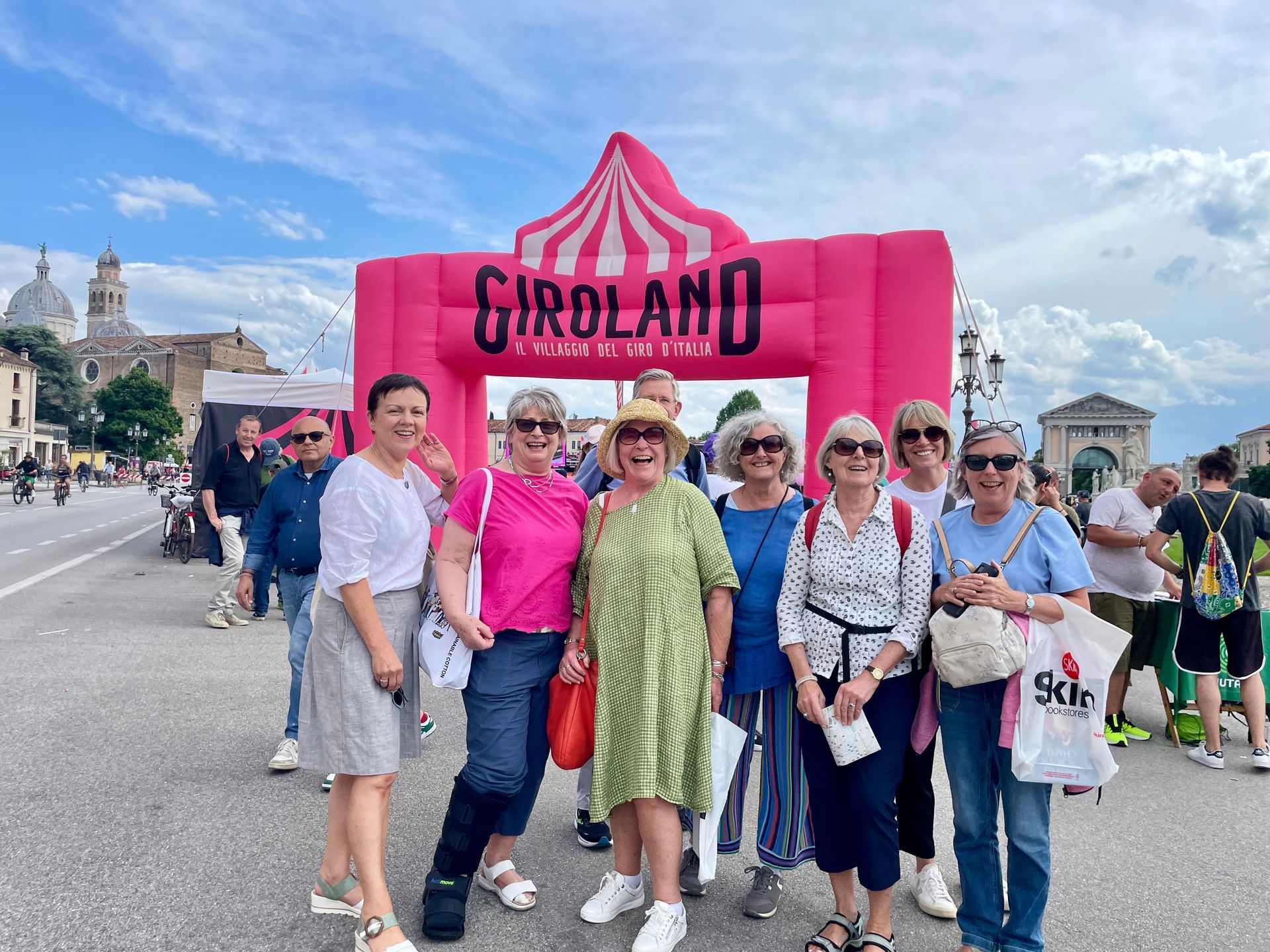 A group of people pose in front of a pink Girolando archway. Sky and buildings in background.