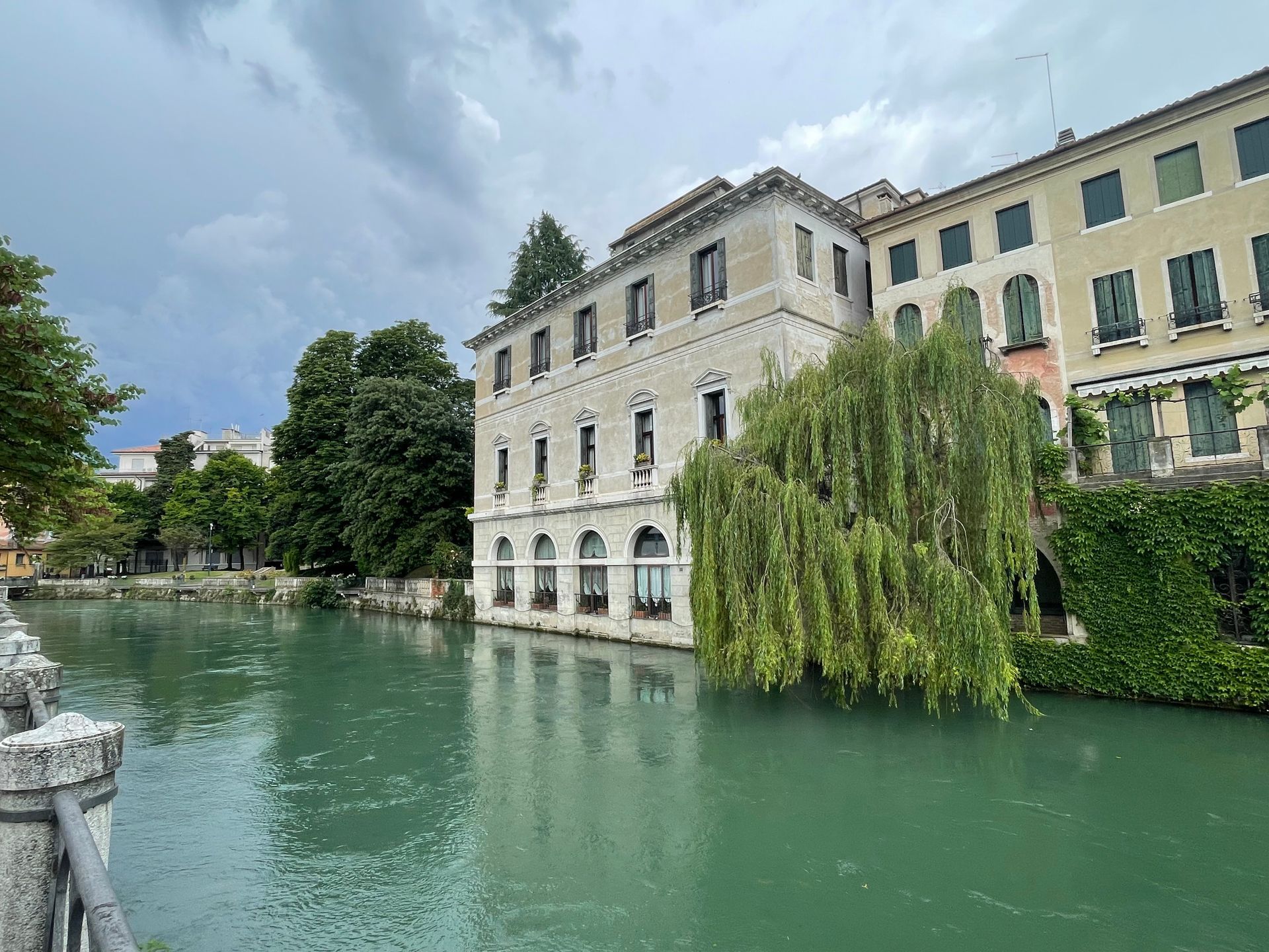 A canal with buildings and trees on the banks under a cloudy sky.