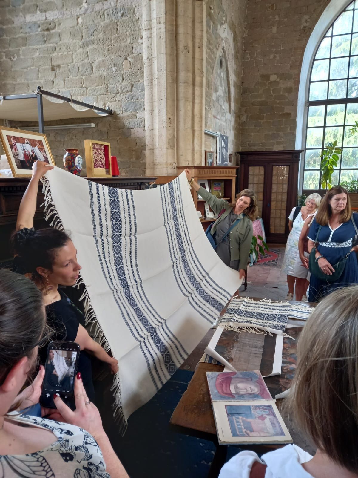 People in a stone room examine a large white textile with blue stripes.