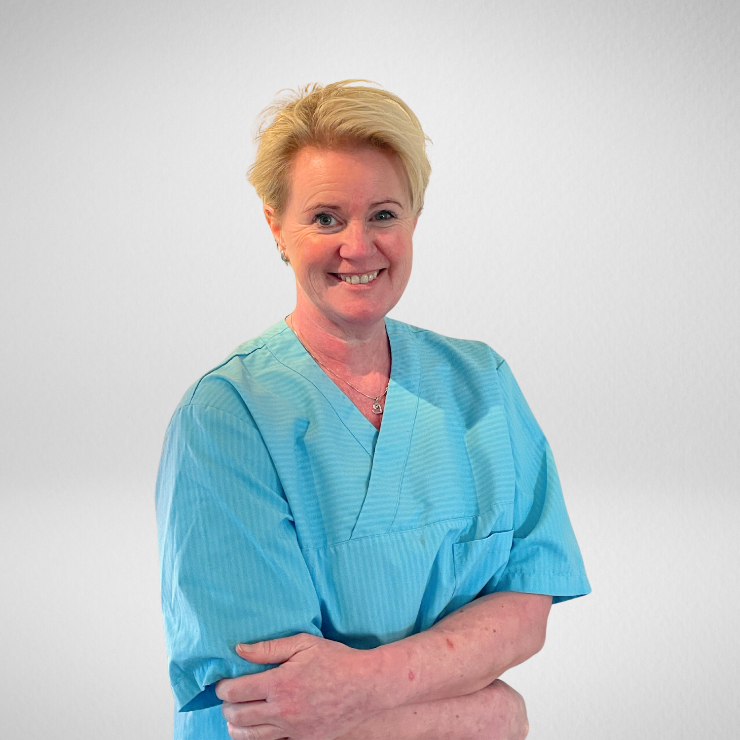 Tannpleier Hege Nordrum i en blå uniform står med armene i kors og smiler.