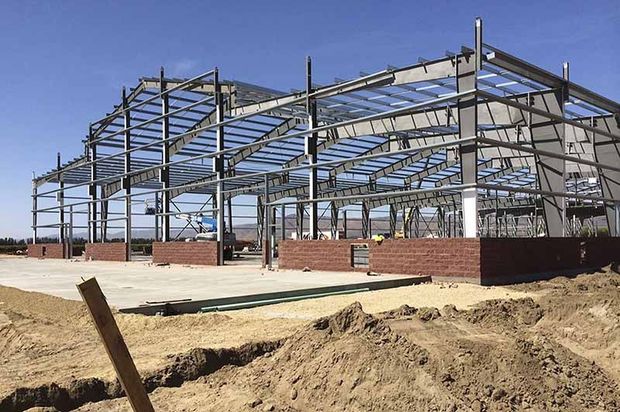 A large metal structure is being built in the middle of a dirt field.