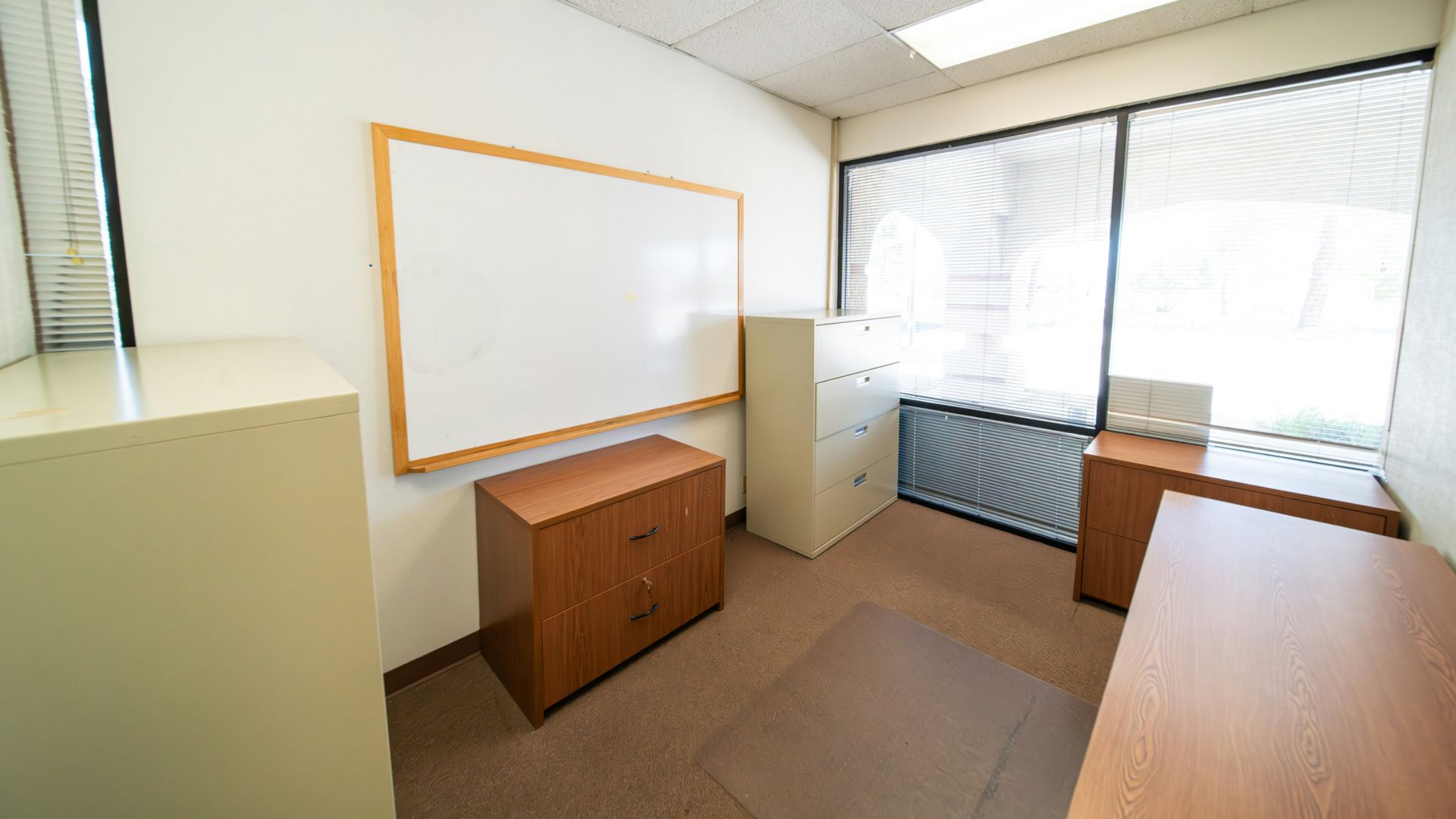 An empty office with various file cabinets and clear whiteboard