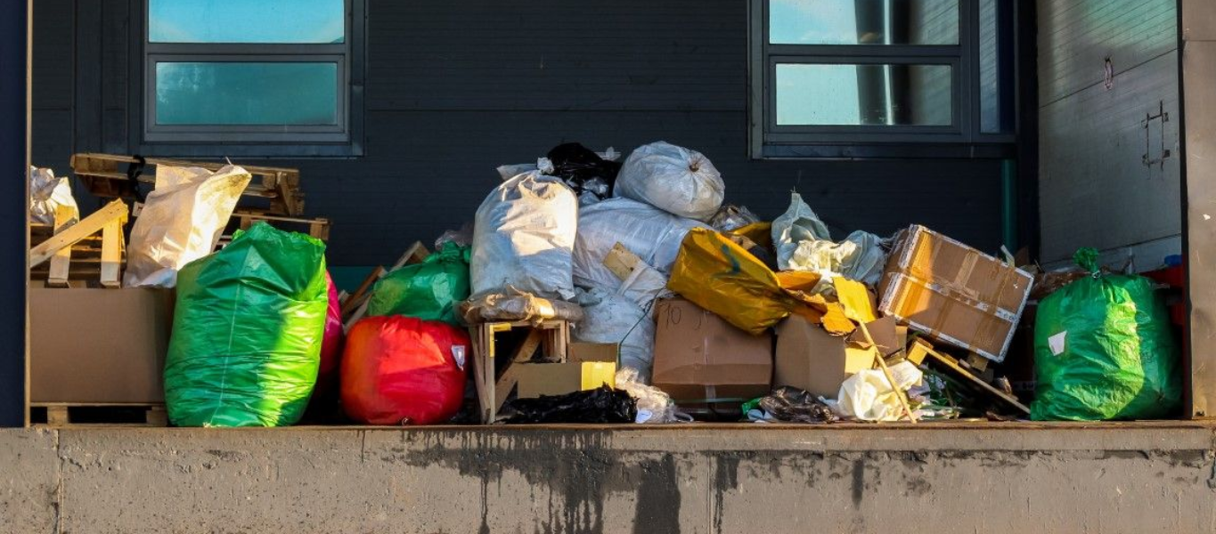 A huge open dumpster with piles of trash bags and smashed boxes lining its top