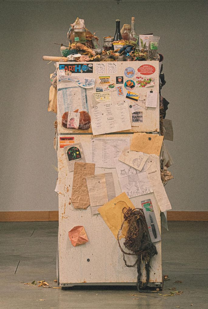 An old refrigerator that is covered in stickers and bits of paper and has junk piled on top of it