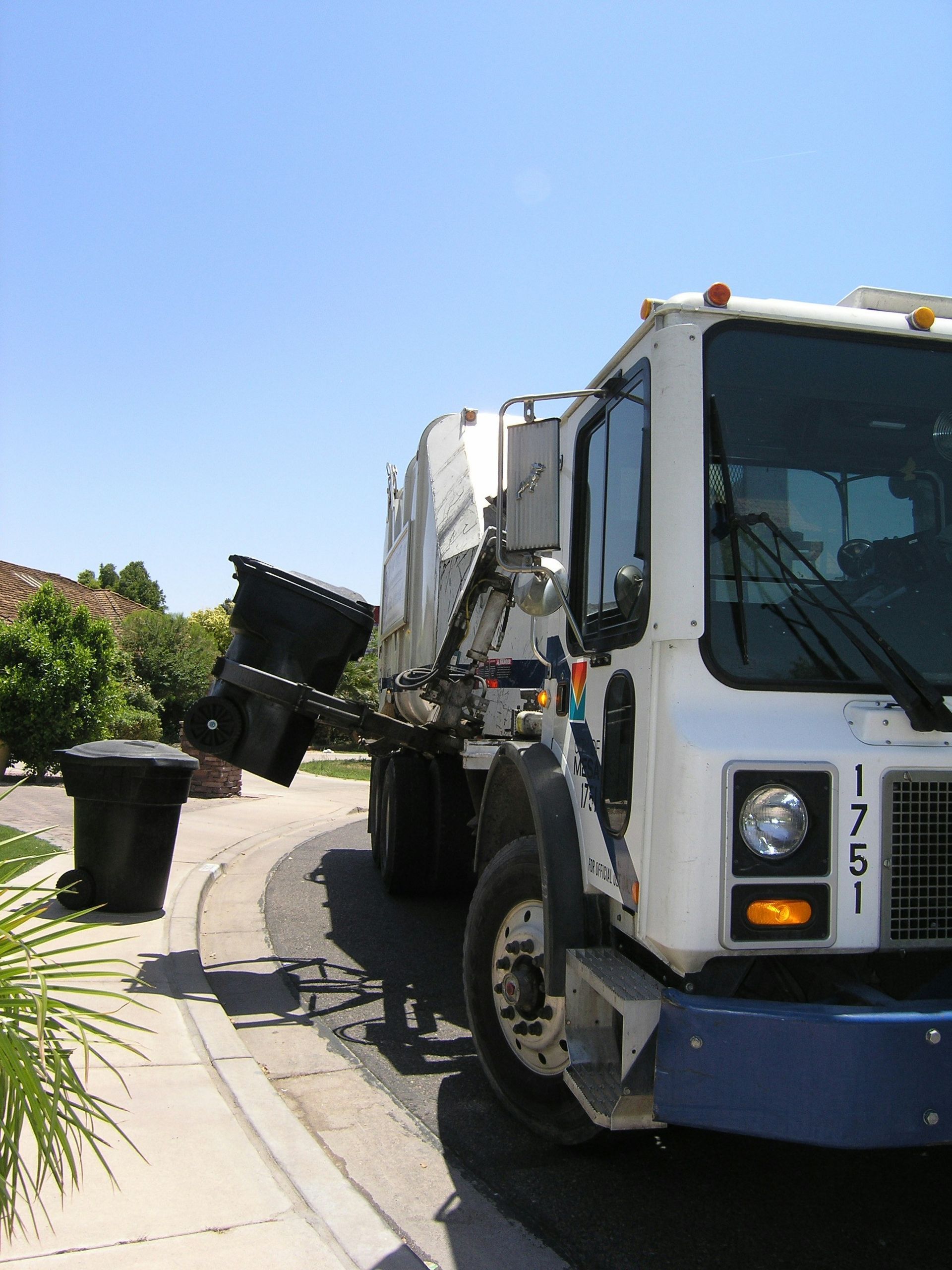 A modern white dump truck in the process of picking up household garbage cans.