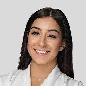 Smiling woman with long dark hair in a white top against a light gray background