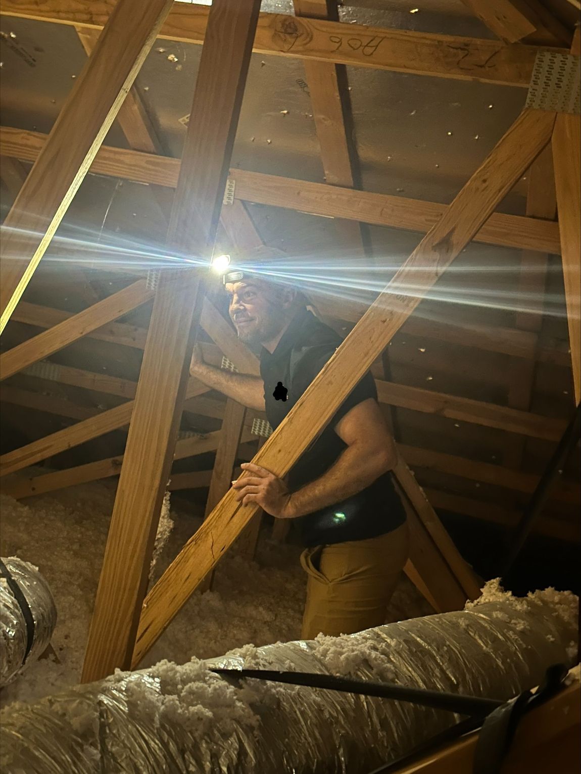 A man is standing in an attic holding a wooden beam.