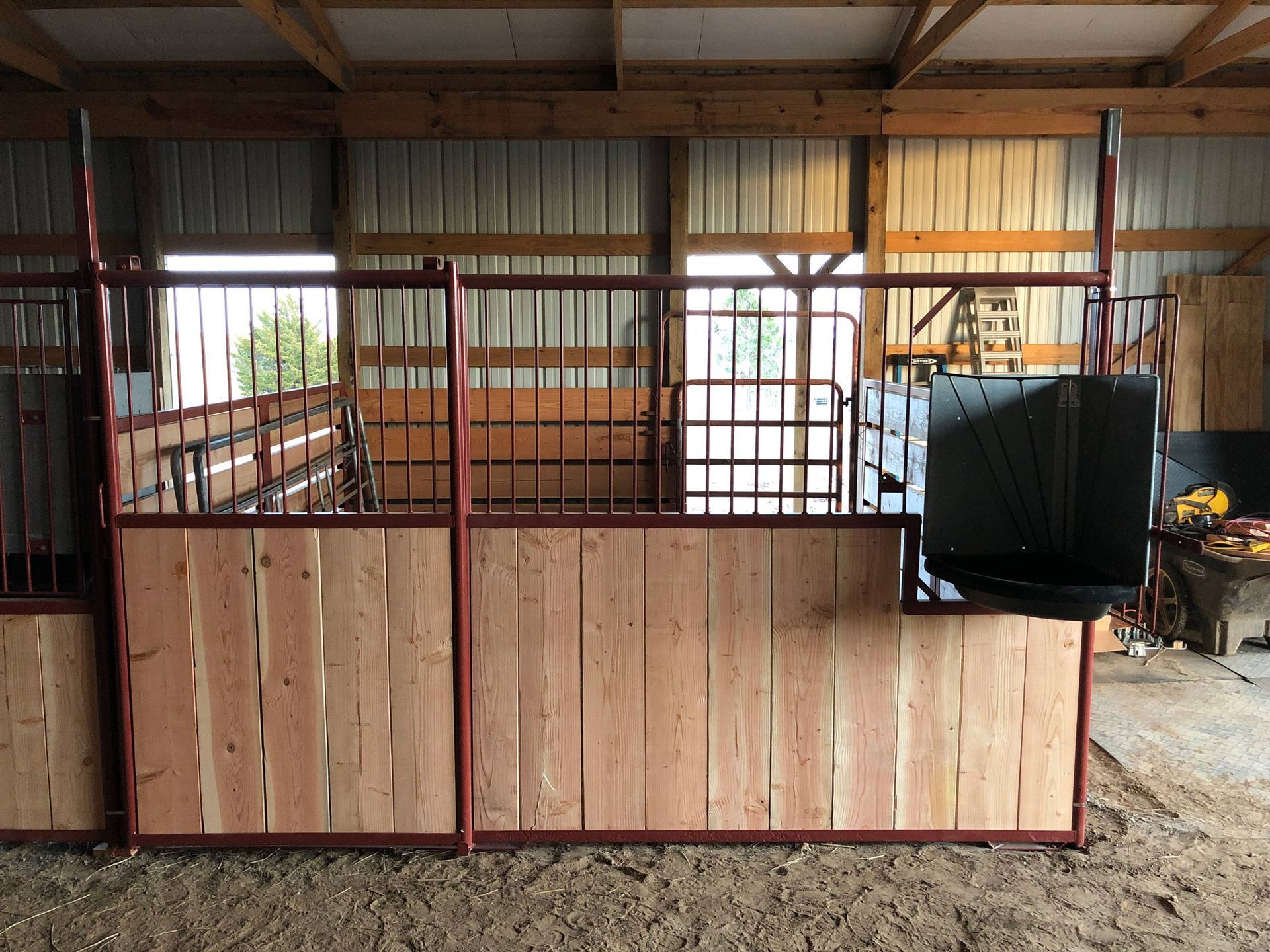 Wooden livestock stall inside a metal-roofed barn, with a black tarp draped over the right side.
