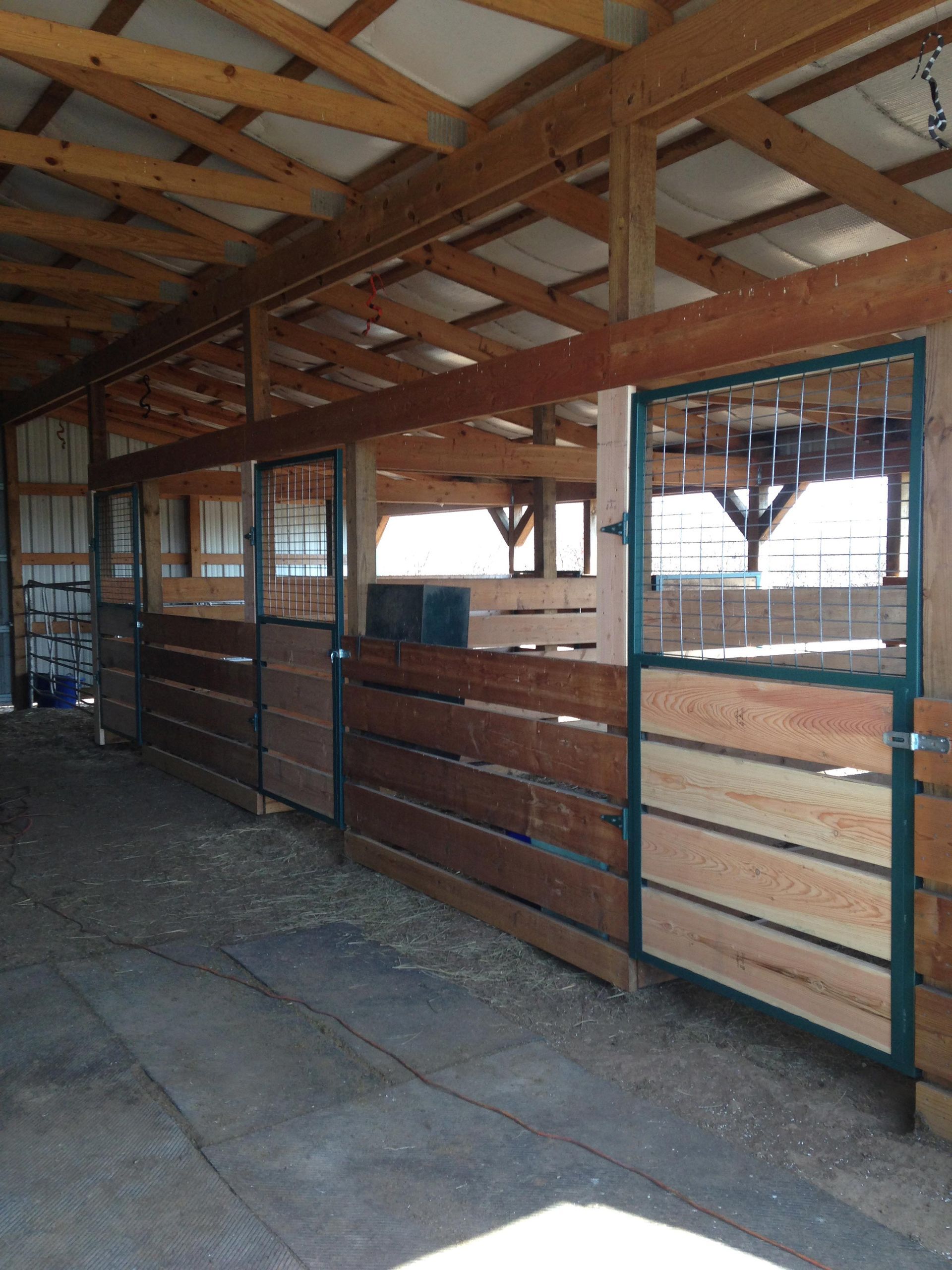 Empty stable interior with wooden stalls, metal gates, and a slanted roof.