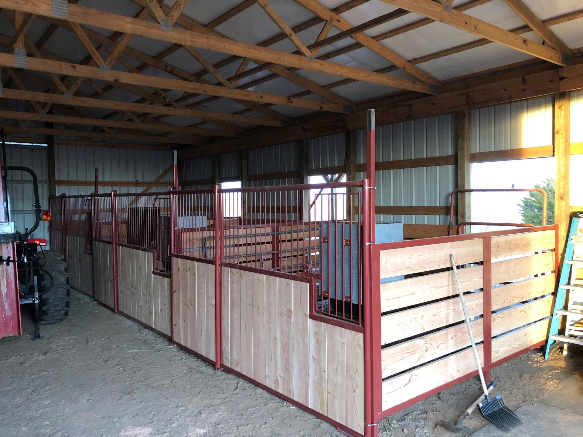 Indoor livestock stalls in a barn with metal fencing and wood panel walls under a wooden roof