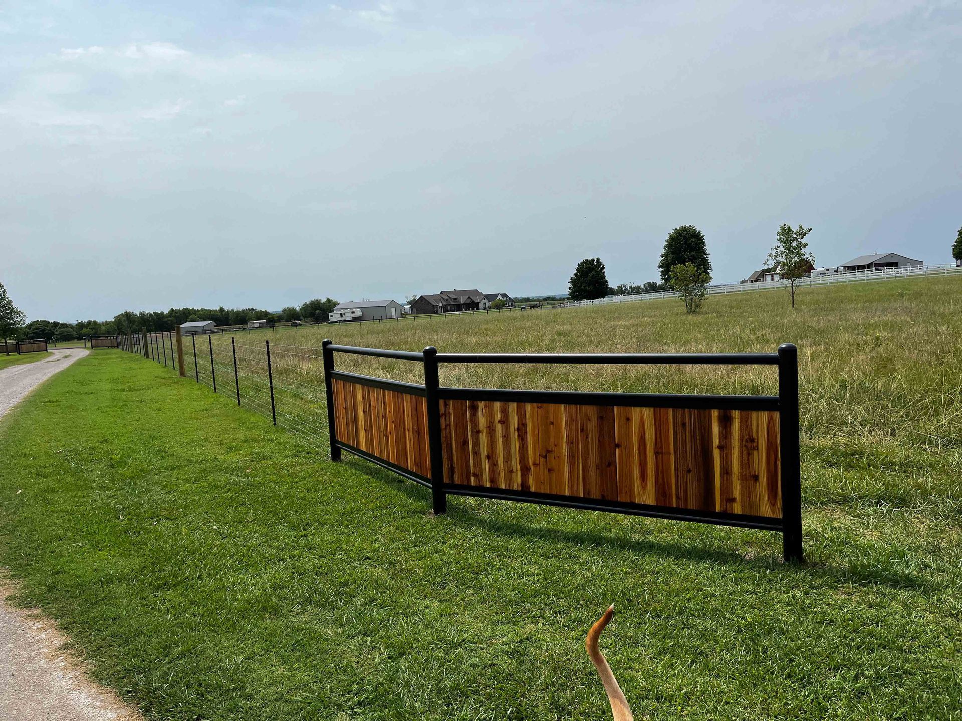 Rural field with a black-and-wood fence beside a grassy path under a cloudy sky