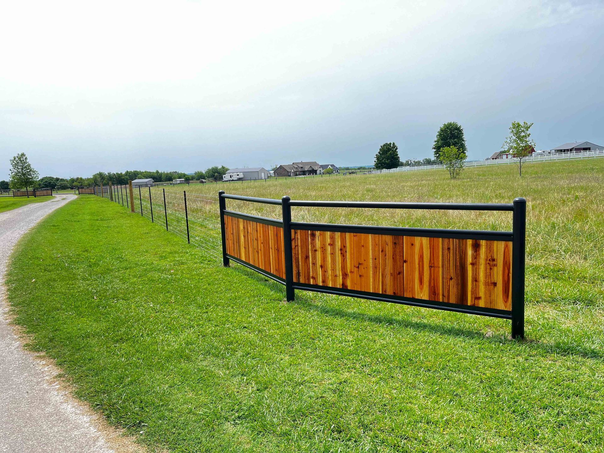 Curved park path beside a black-post wooden fence on a grassy field under an overcast sky