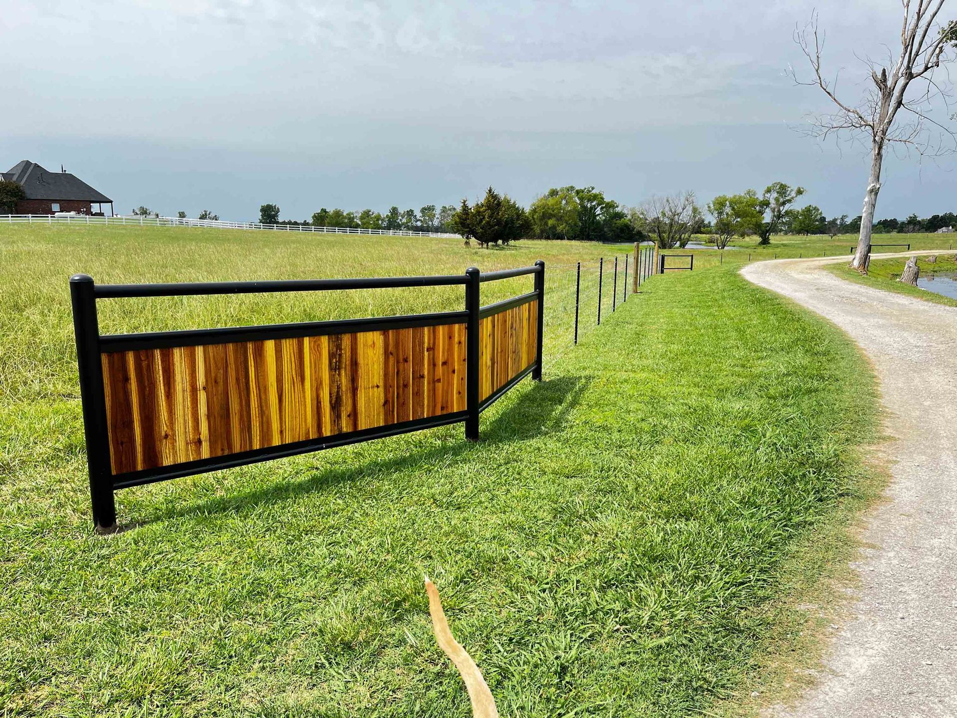 Wooden fence beside a curving gravel path in a green field under a cloudy sky