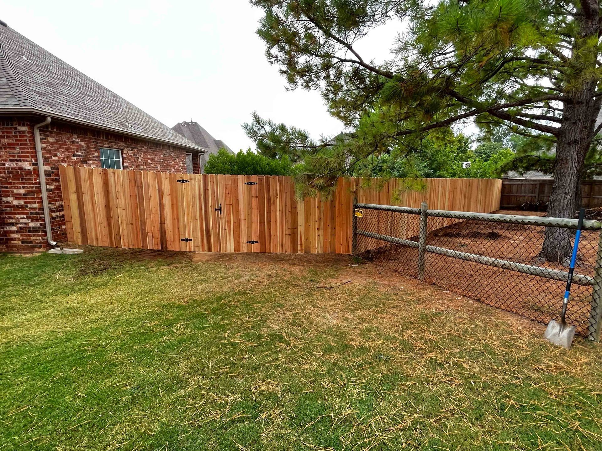Backyard with wooden privacy fence, chain-link fence, grass, brick house, and trees