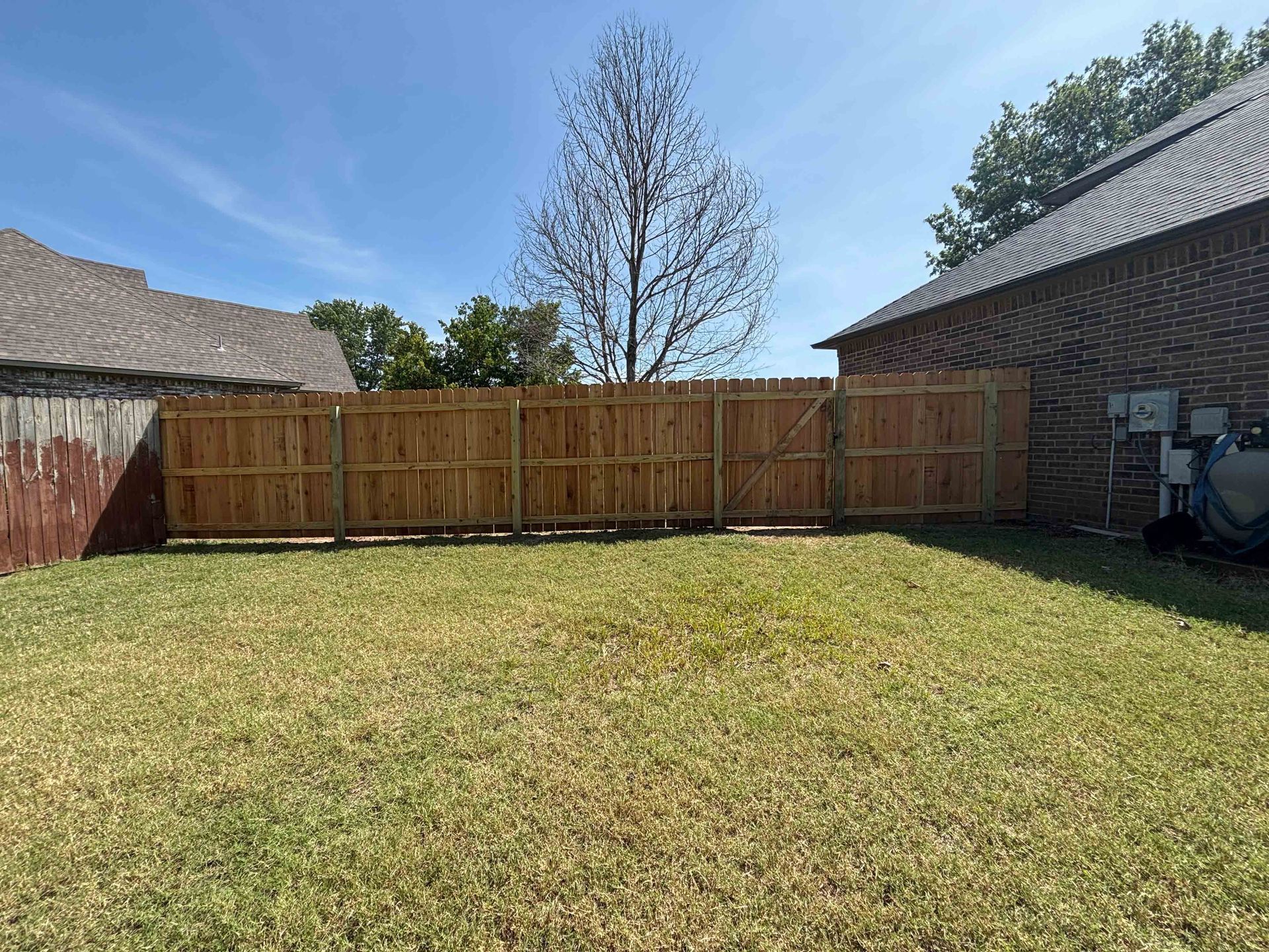 Backyard with a wooden fence between two brick houses under a clear sky.