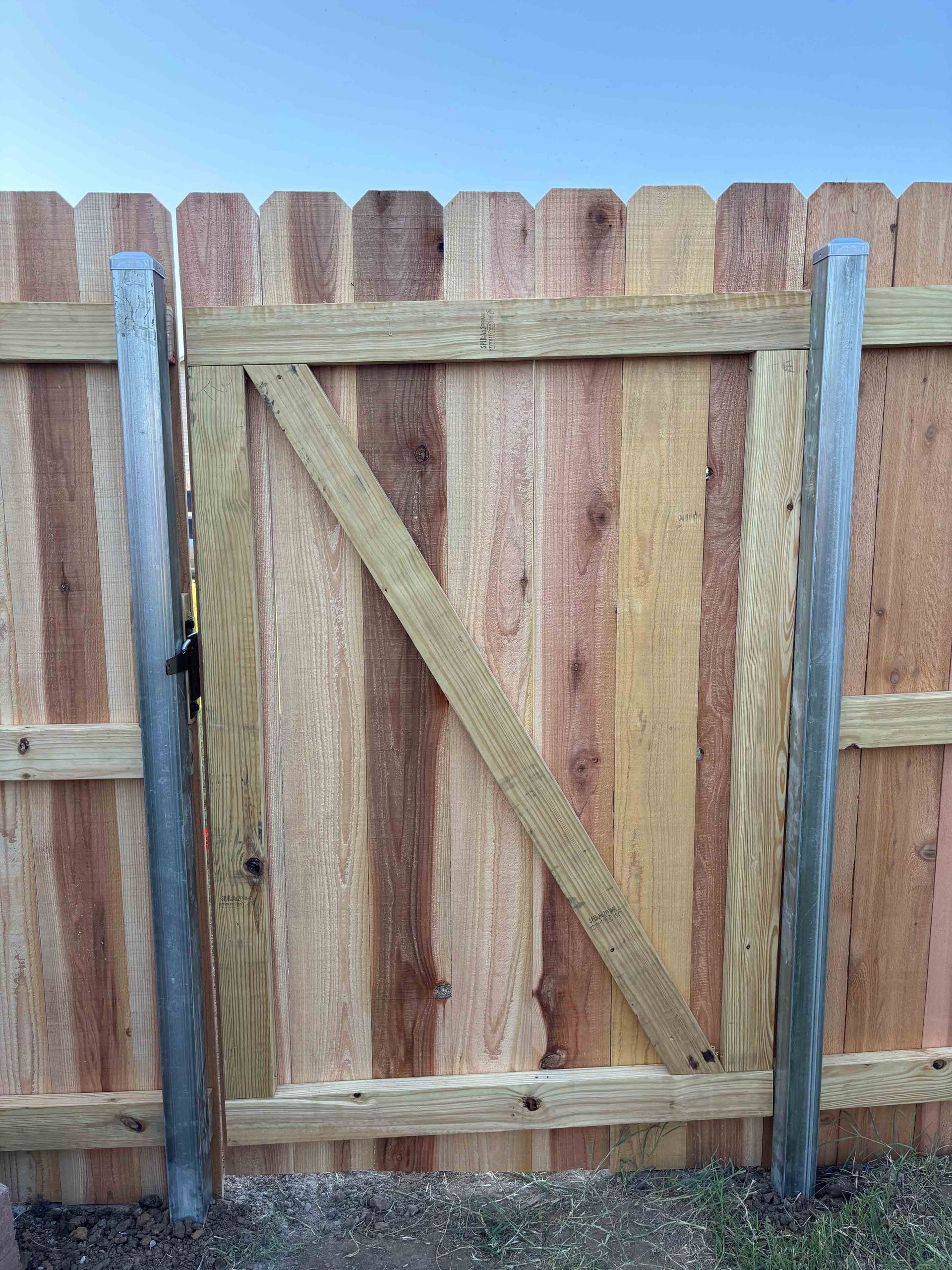 Wooden backyard fence gate with diagonal brace between two blue-gray posts