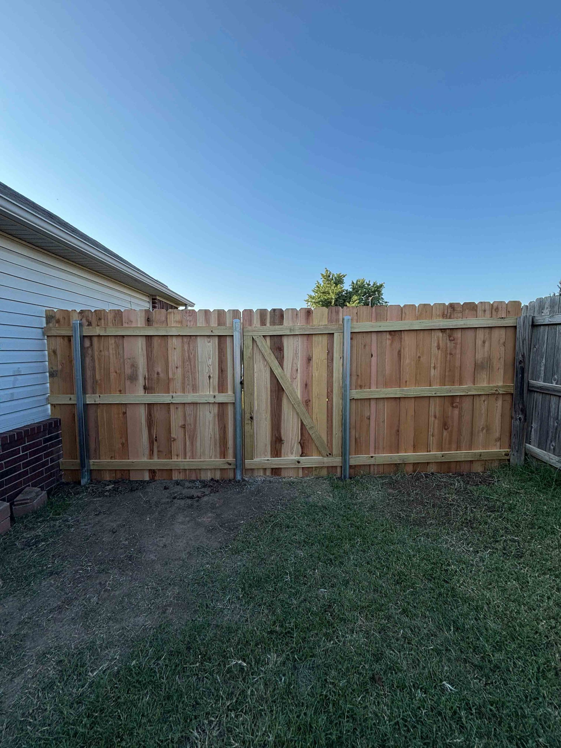 Backyard wooden privacy fence beside a house under a clear blue sky