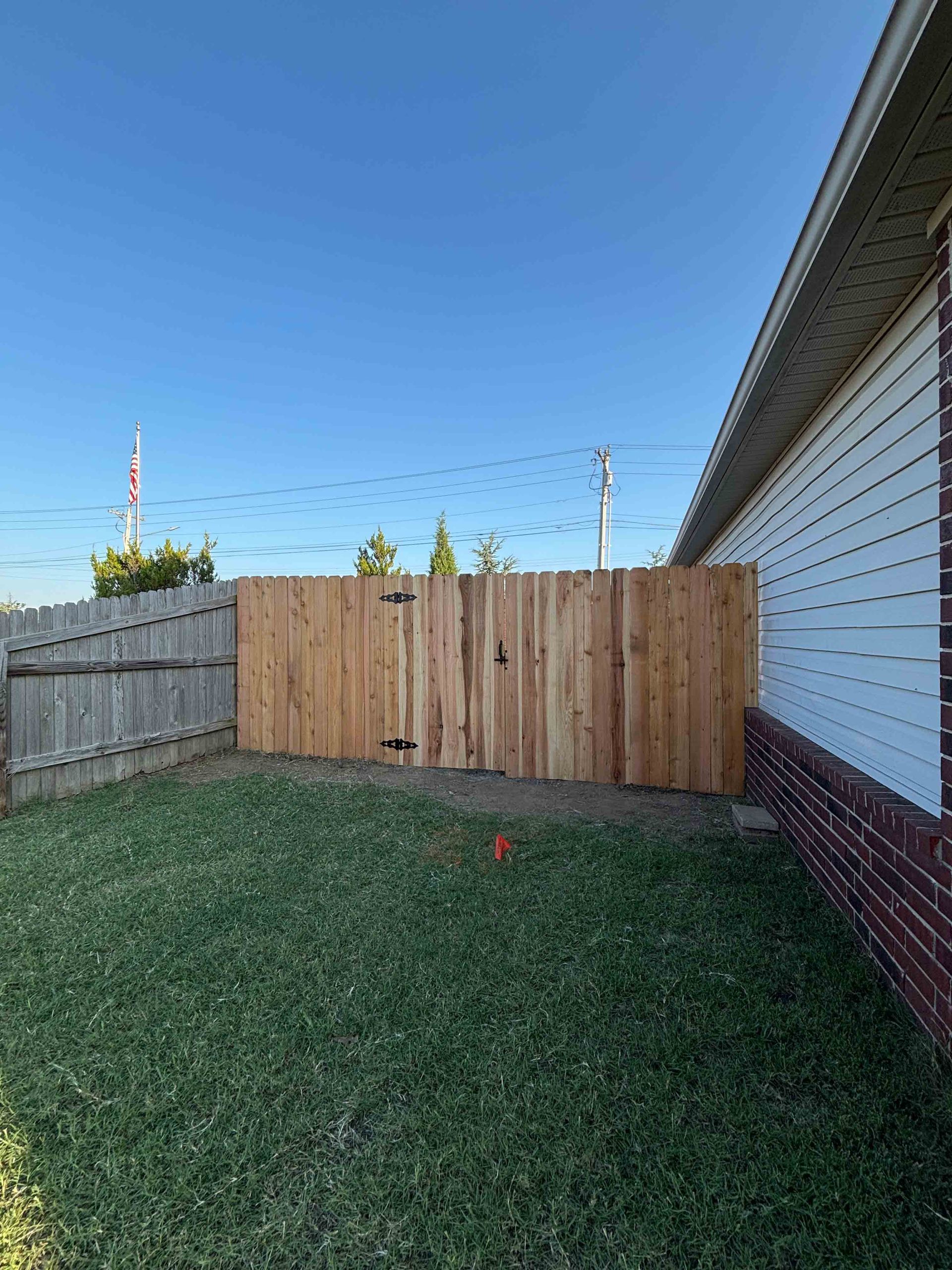 Backyard with a wooden fence, grass lawn, and the side of a house under a clear blue sky