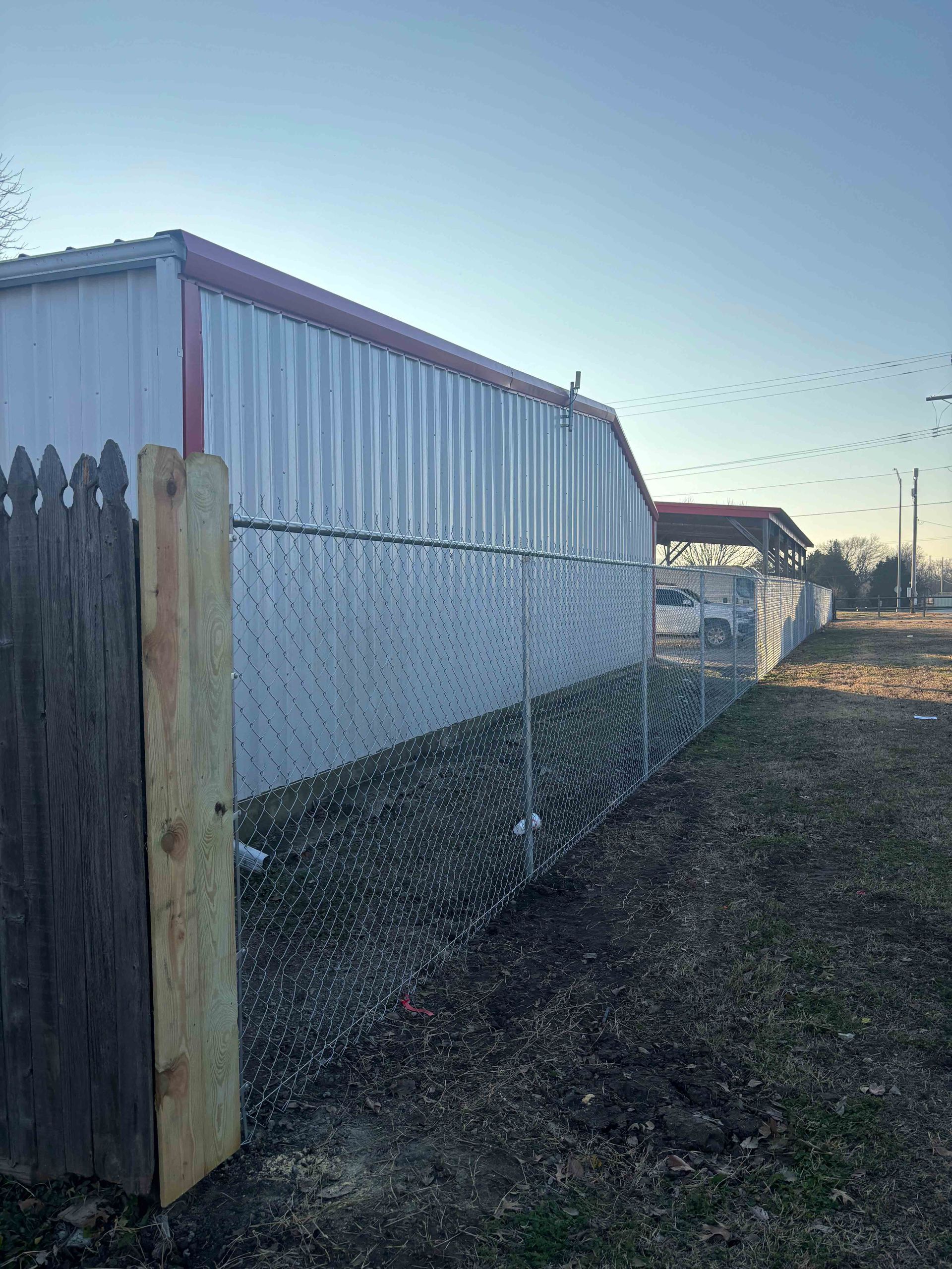 Chain-link fence beside a white-sided building at sunset, with a wooden post in the foreground.