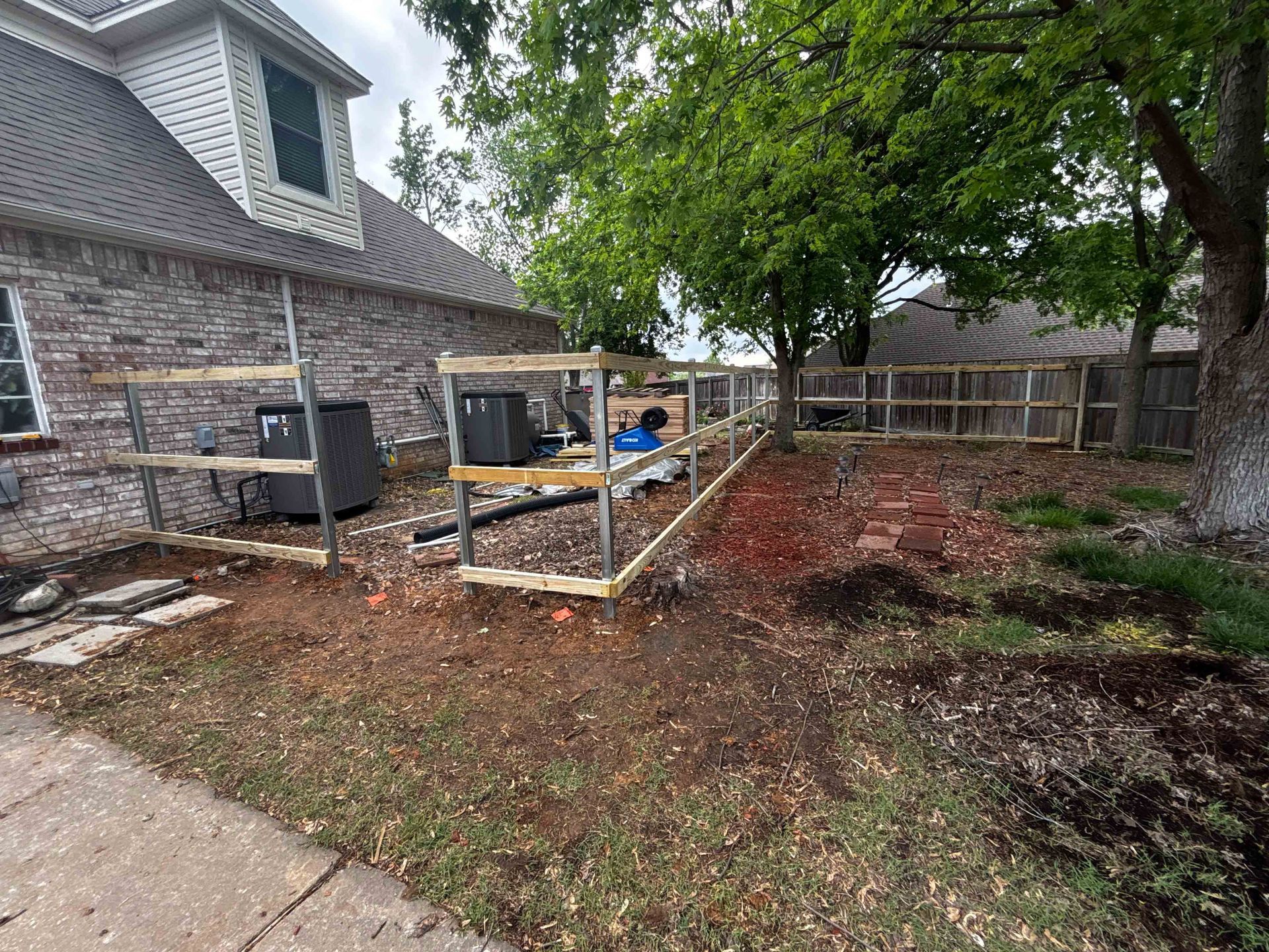Backyard with new raised garden beds beside a brick house and large tree