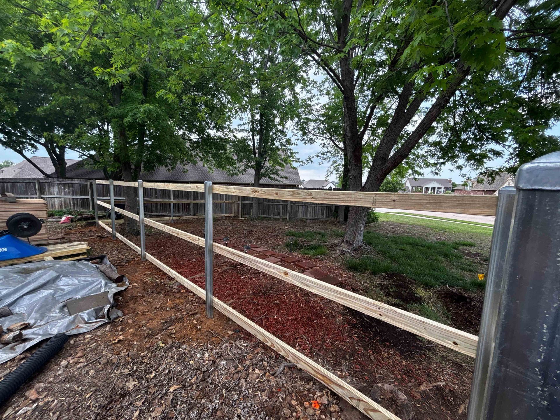 Wooden fence along a dirt path under a tree in a backyard garden area