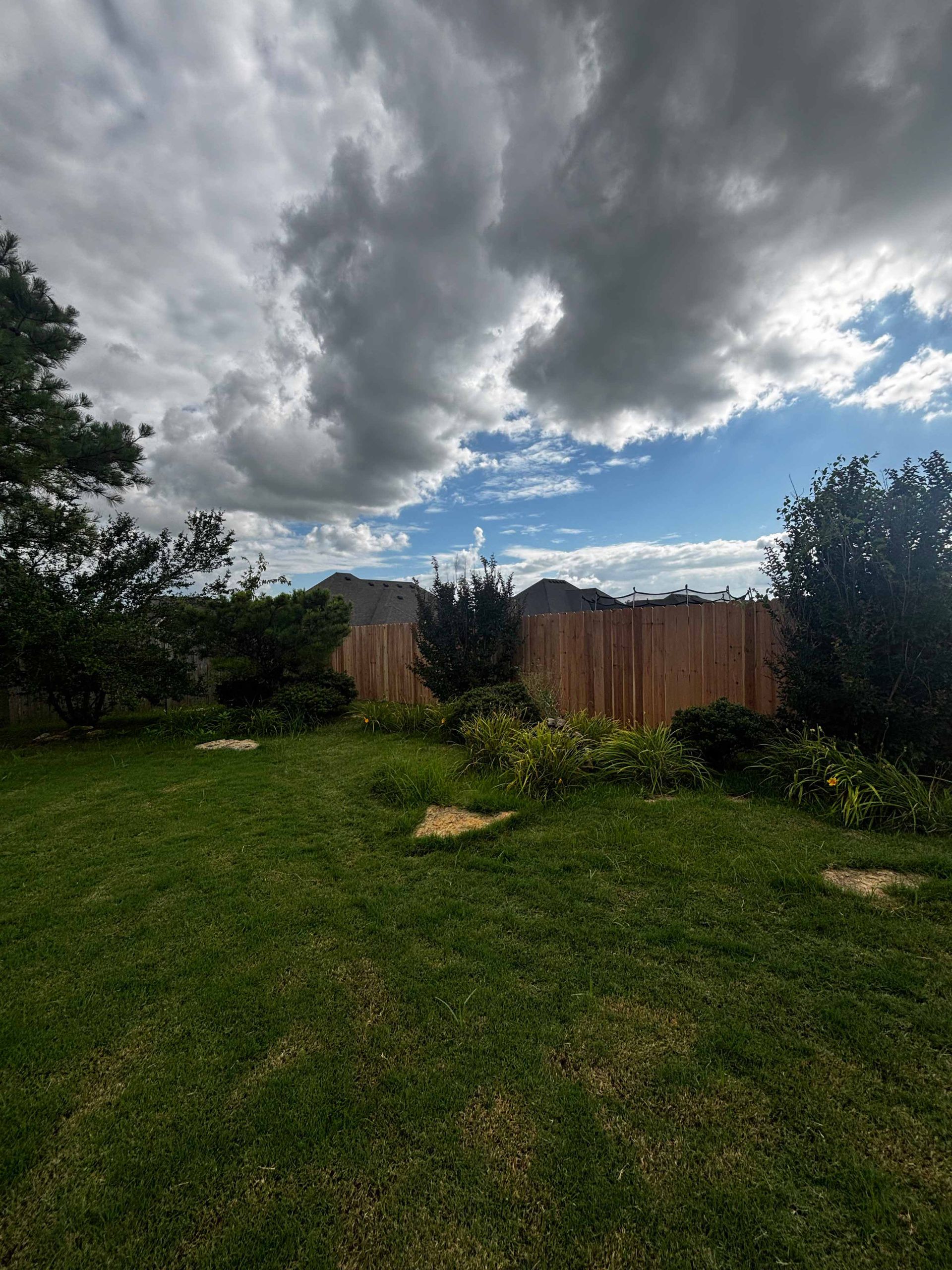 Grassy backyard under dark storm clouds, with a wooden fence and trees along the edges