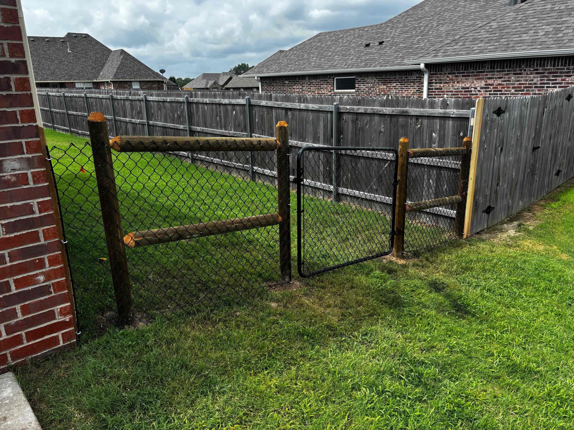 Backyard with a small fenced grass area beside a brick house and wooden privacy fences