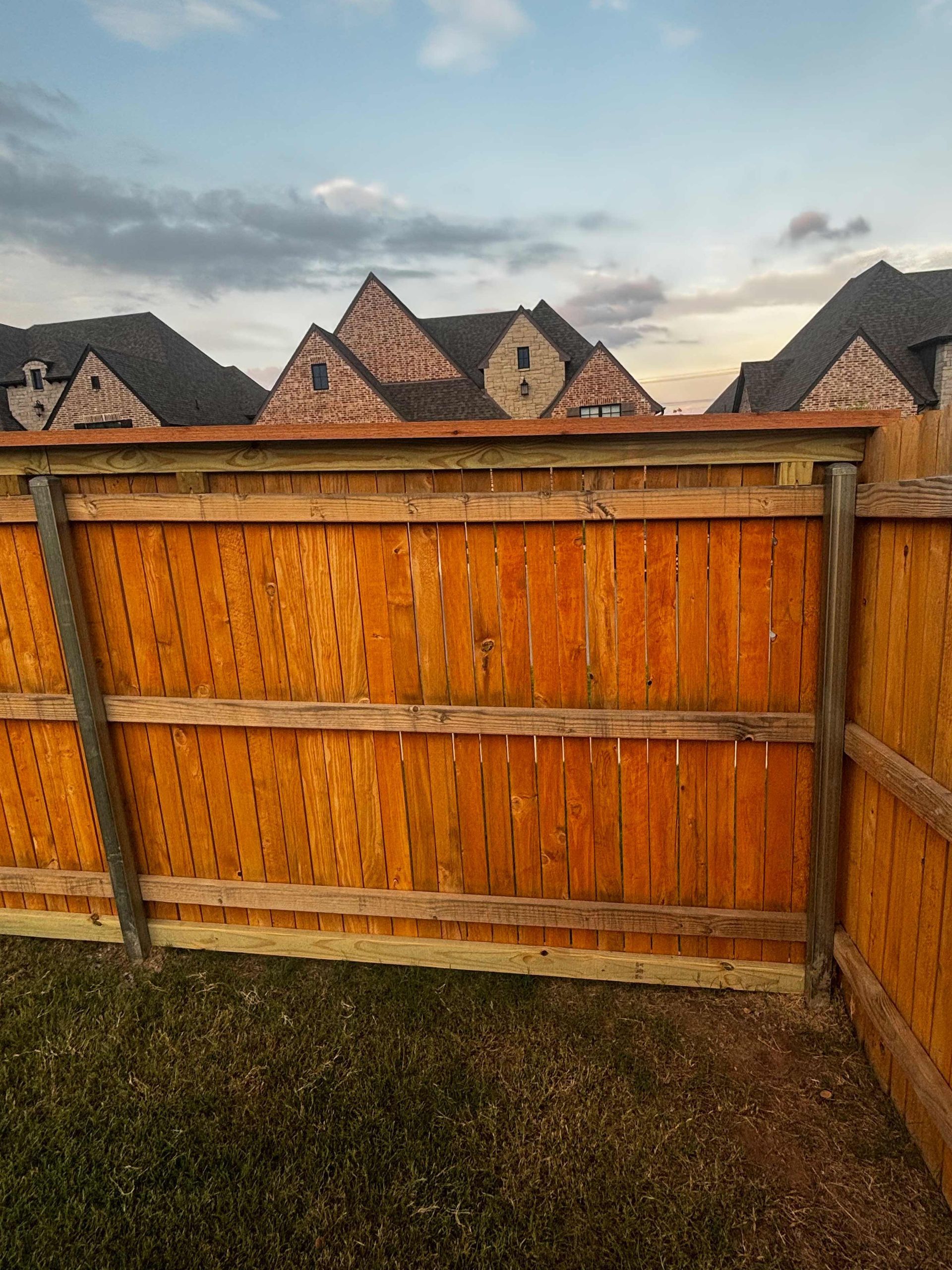 Wooden backyard fence with neighboring rooftops and cloudy sky beyond