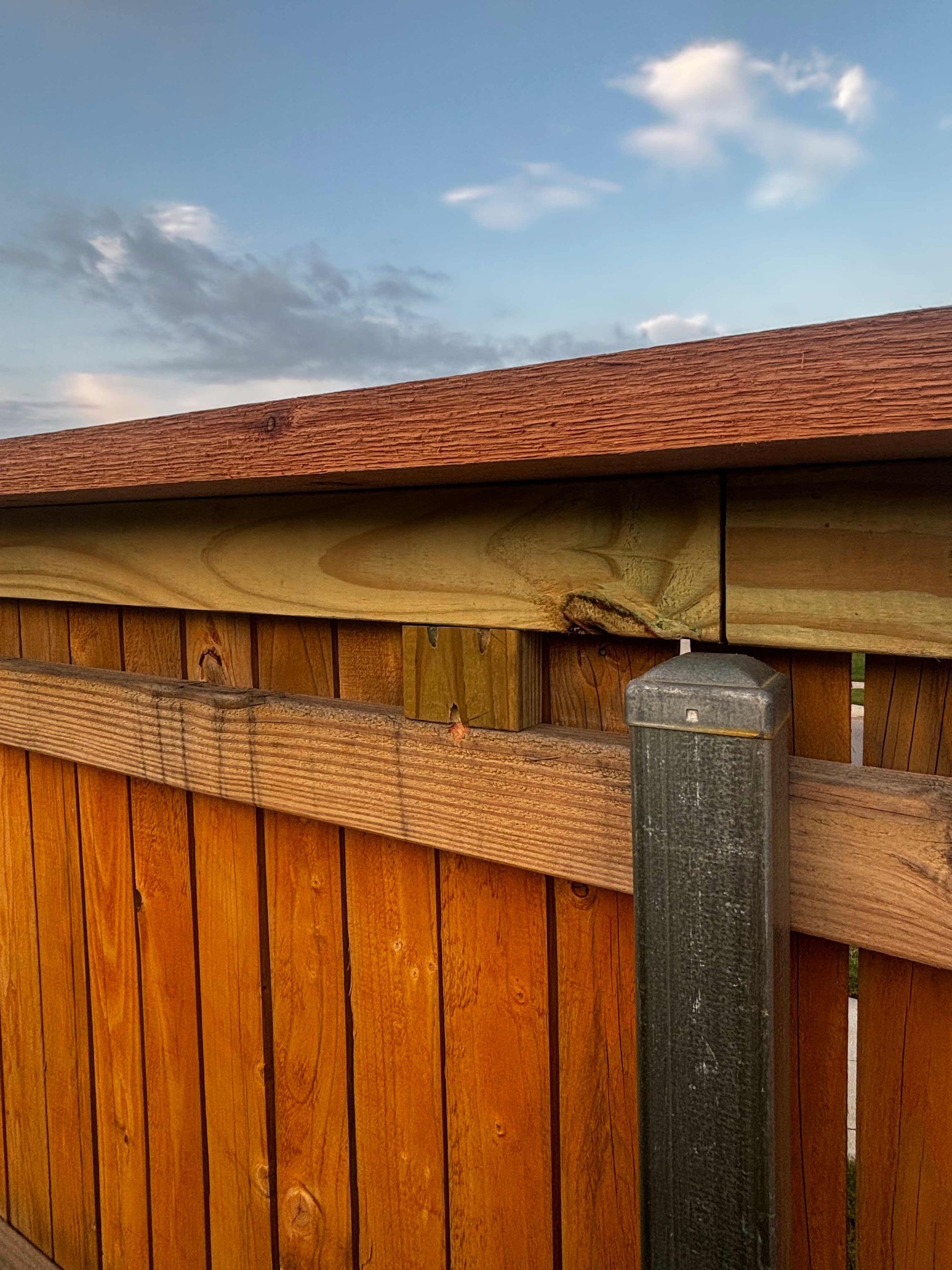Wooden fence with red-tiled roof and metal post under a cloudy blue sky