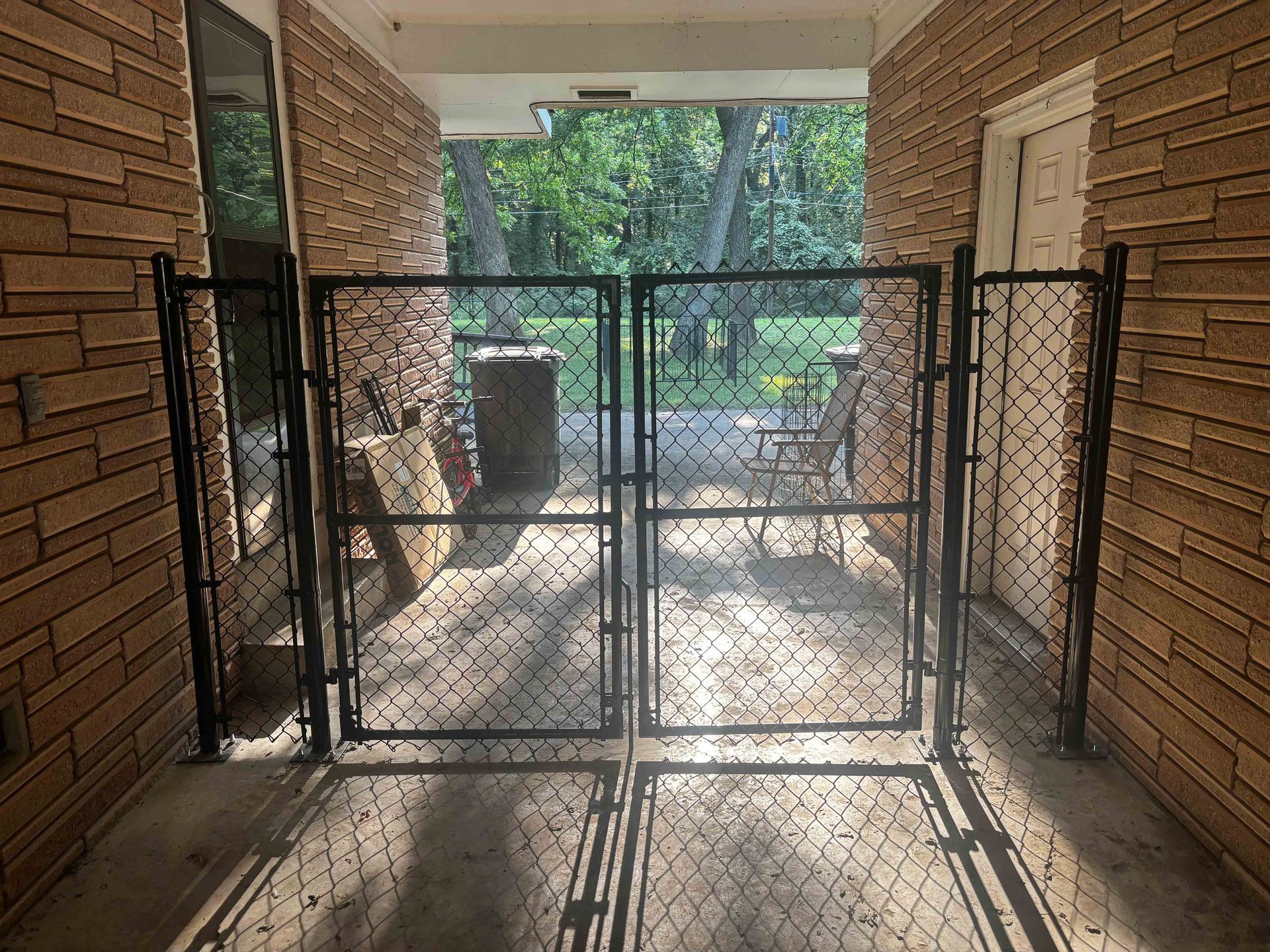 Chain-link gate blocking a brick apartment breezeway with sunlight and trees beyond
