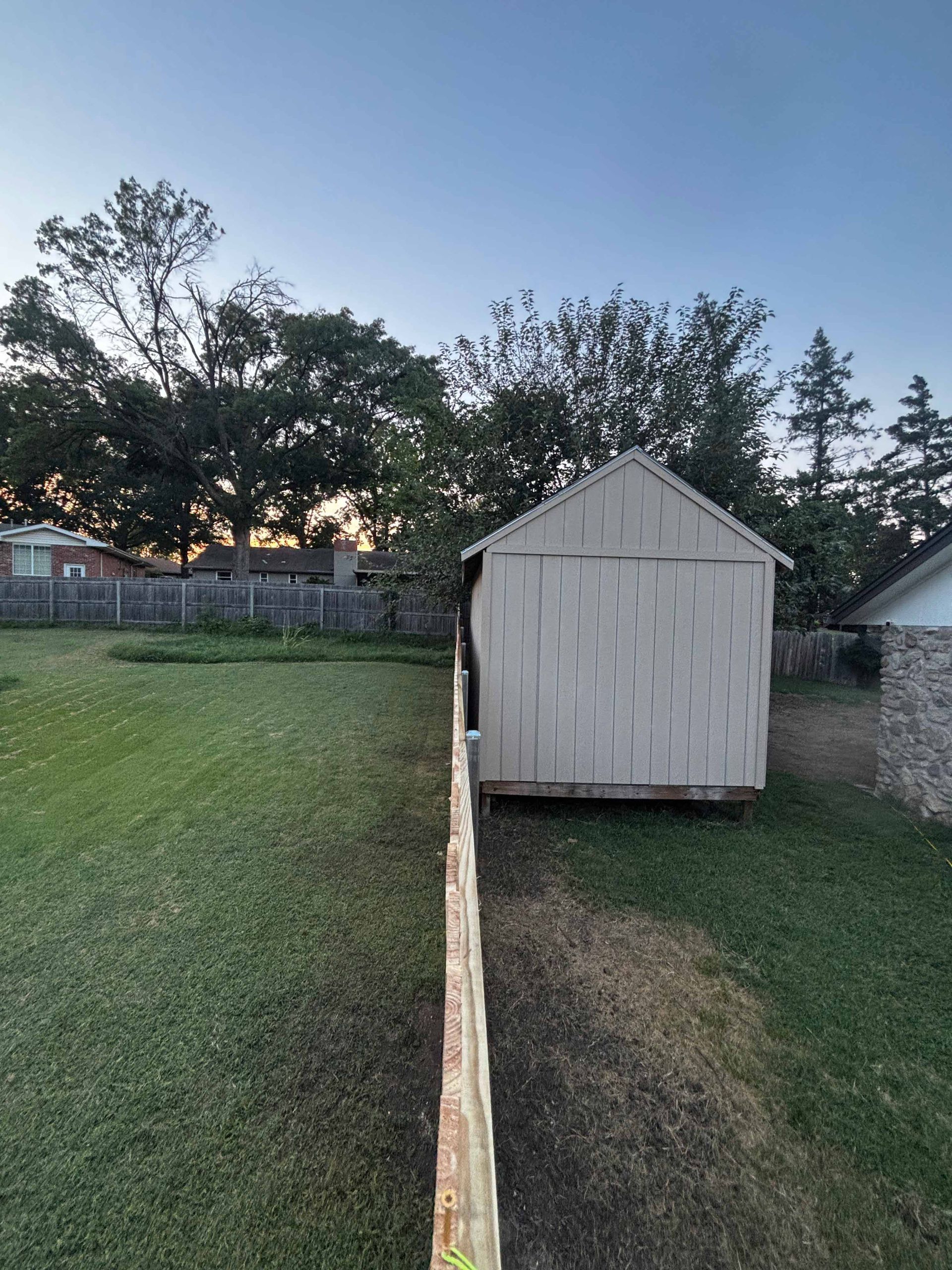 Backyard with a small white shed beside a chain-link fence at dusk