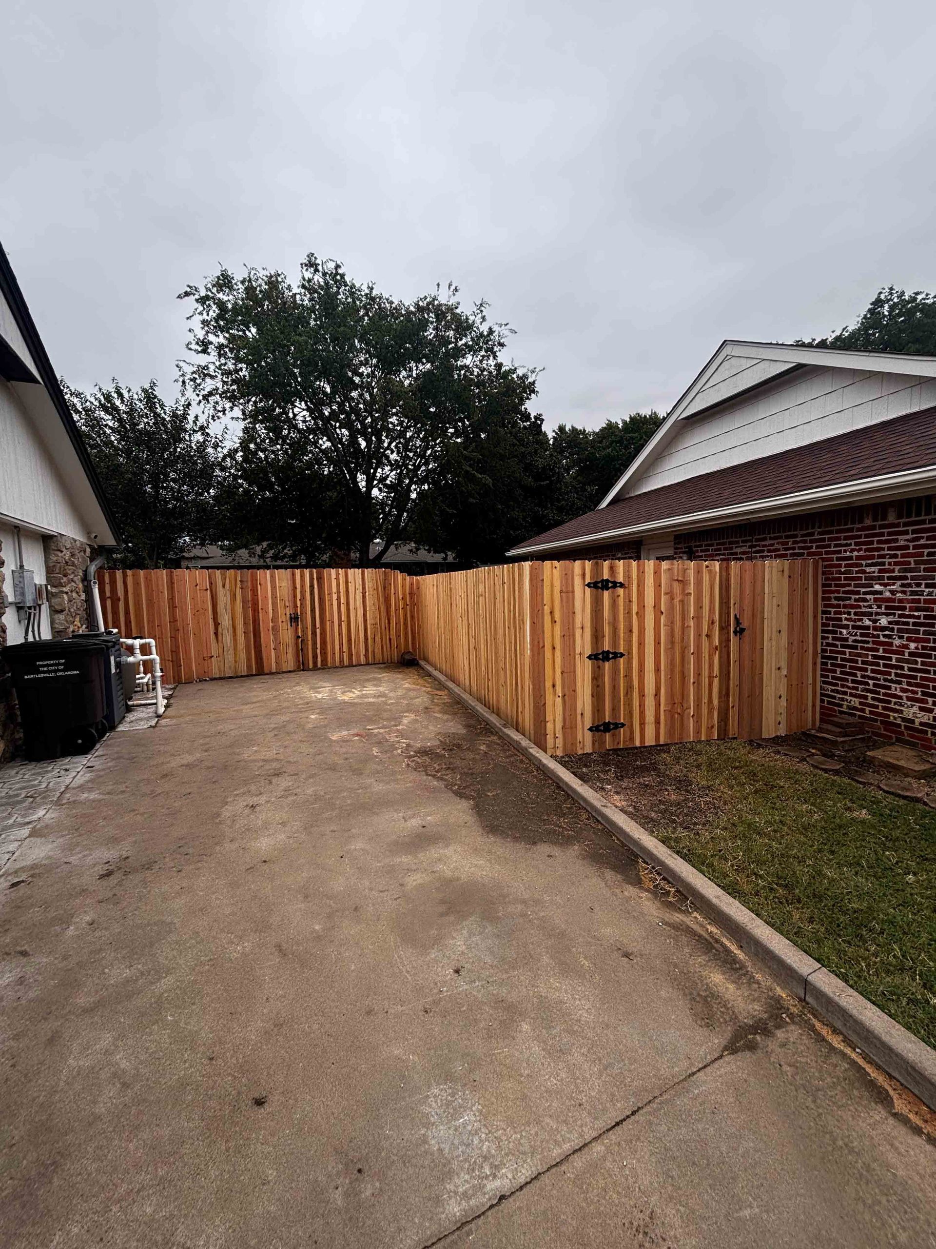 Driveway beside a wooden privacy fence and house under a cloudy sky.