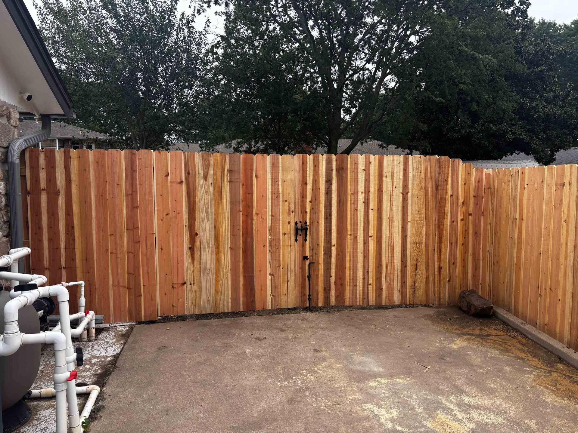 Small fenced backyard with a wooden gate, concrete patio, and pool equipment on the left.