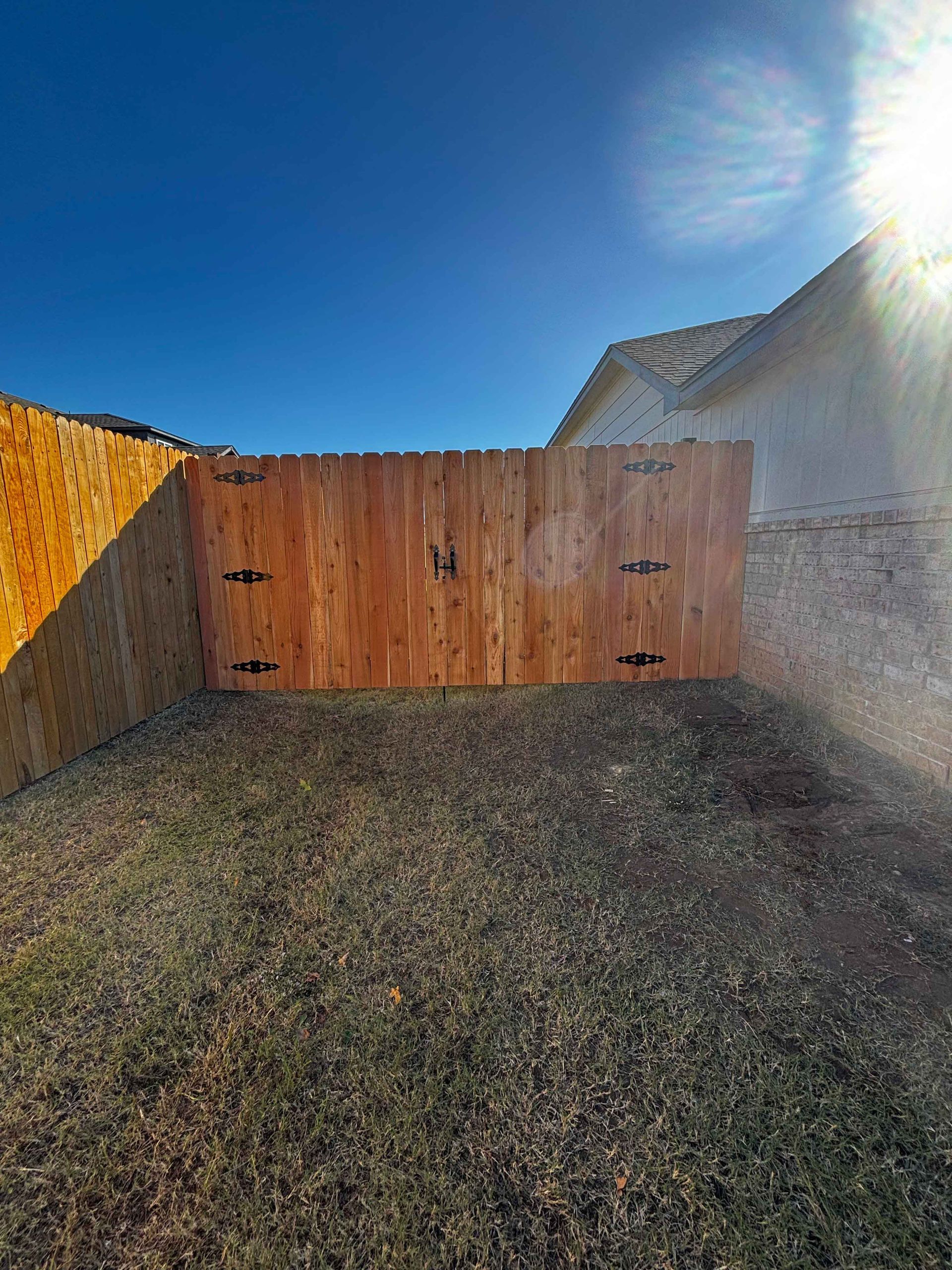 Wooden gate at the end of a gravel driveway, with bright sun and blue sky overhead.