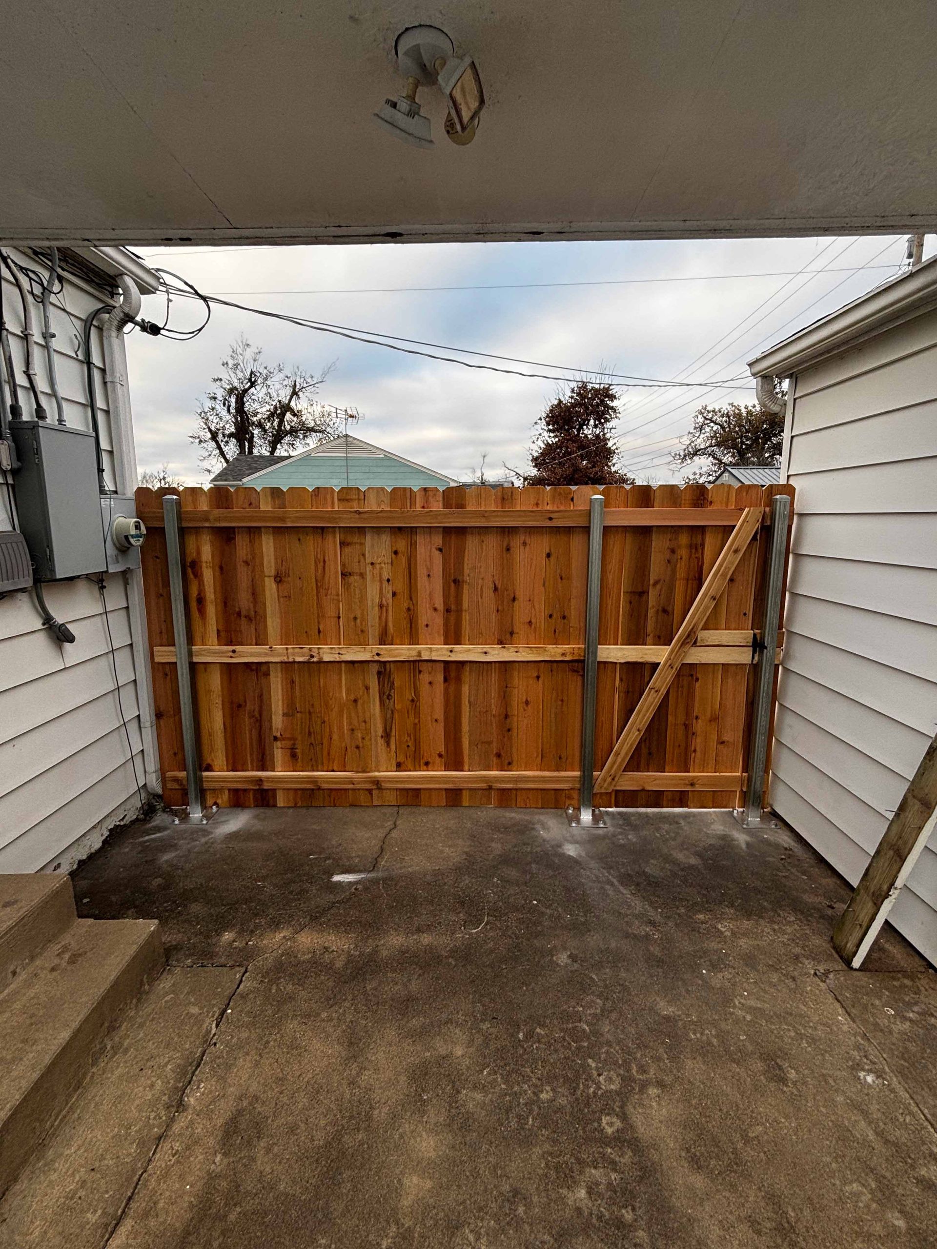 Concrete driveway with a wooden gate between two white-sided buildings under an overhang