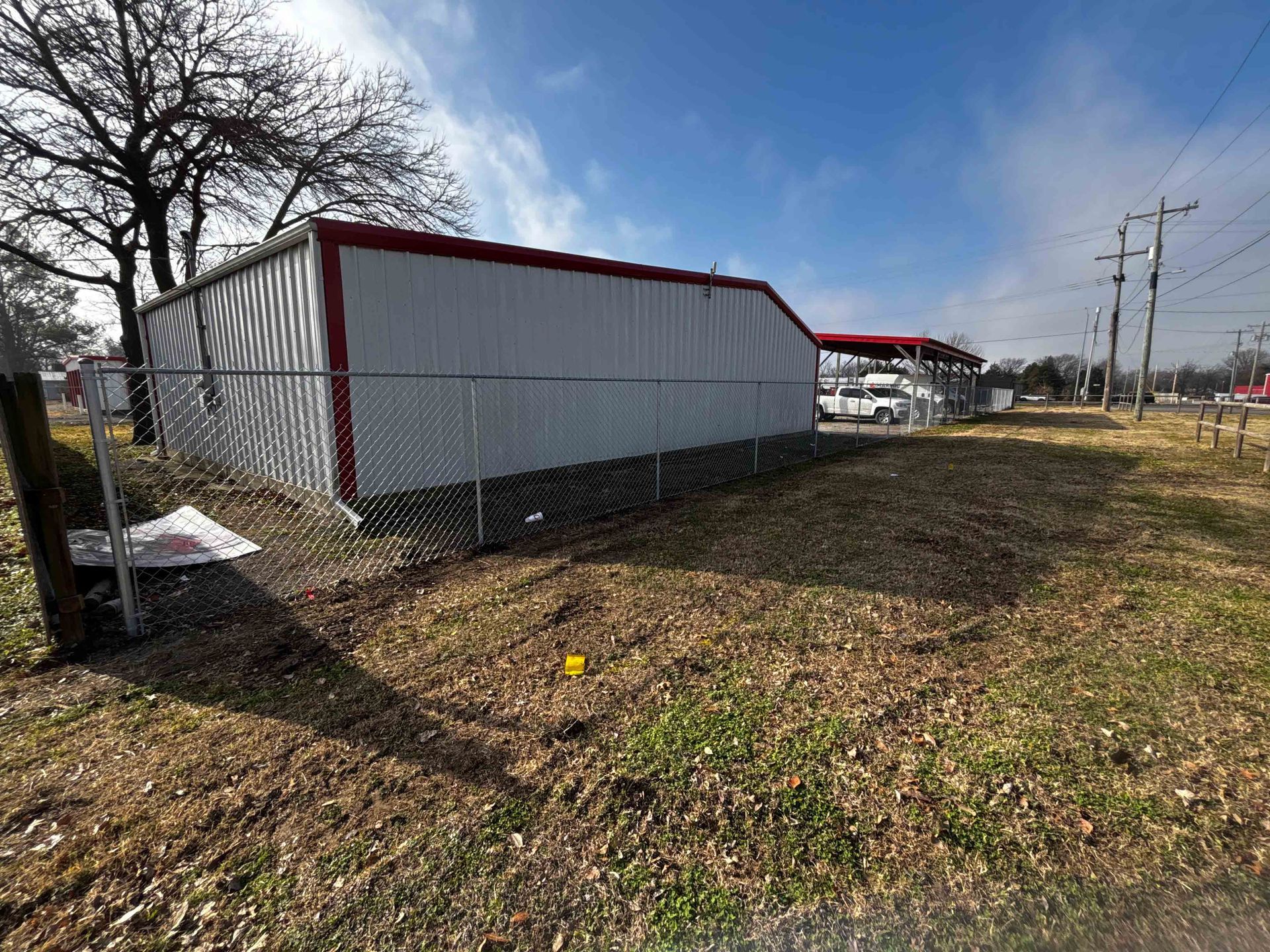White storage building with red trim in a grassy lot beside a fence under a cloudy sky.