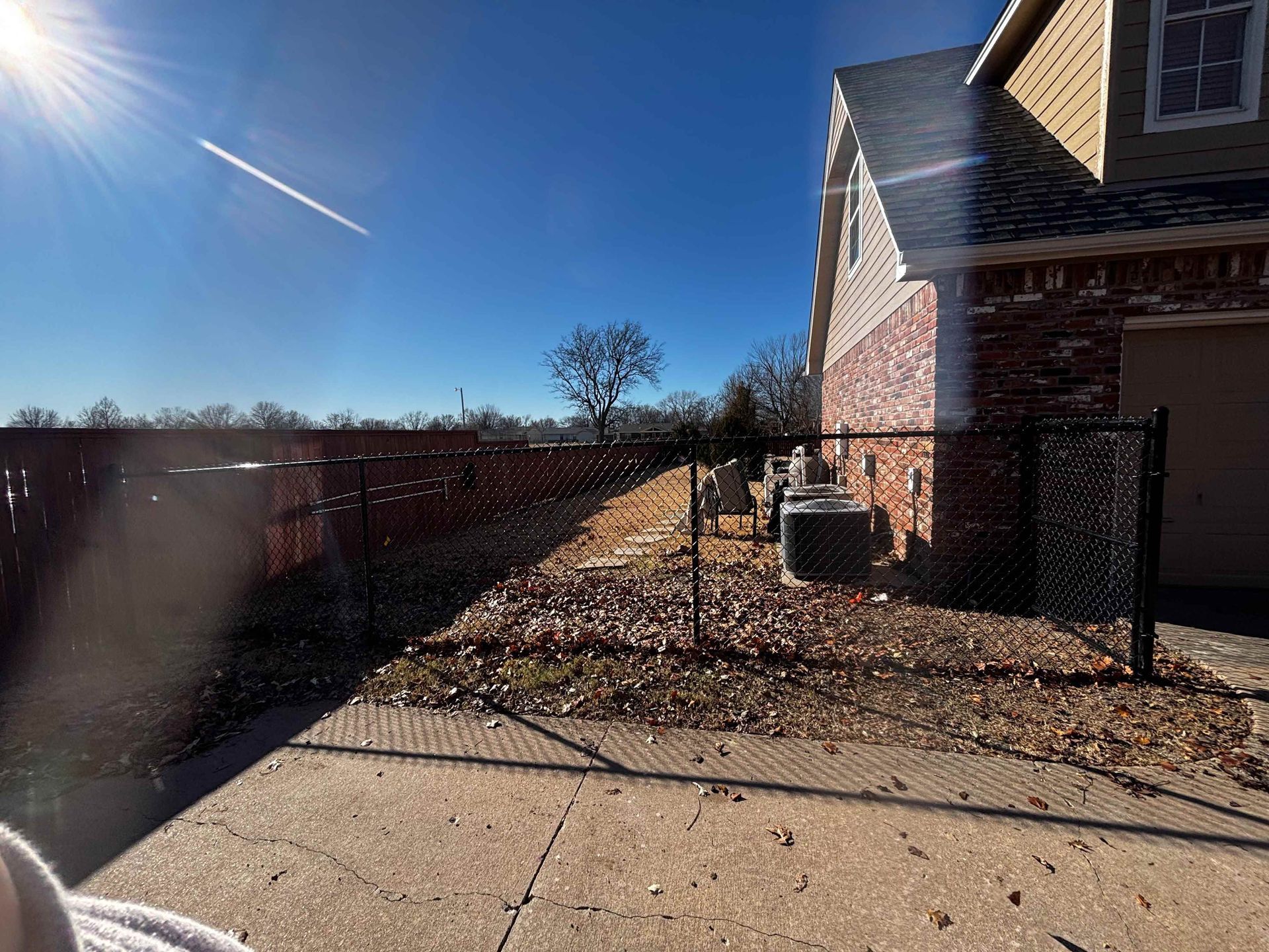 Backyard beside a brick house with a fenced side yard under a clear blue sky