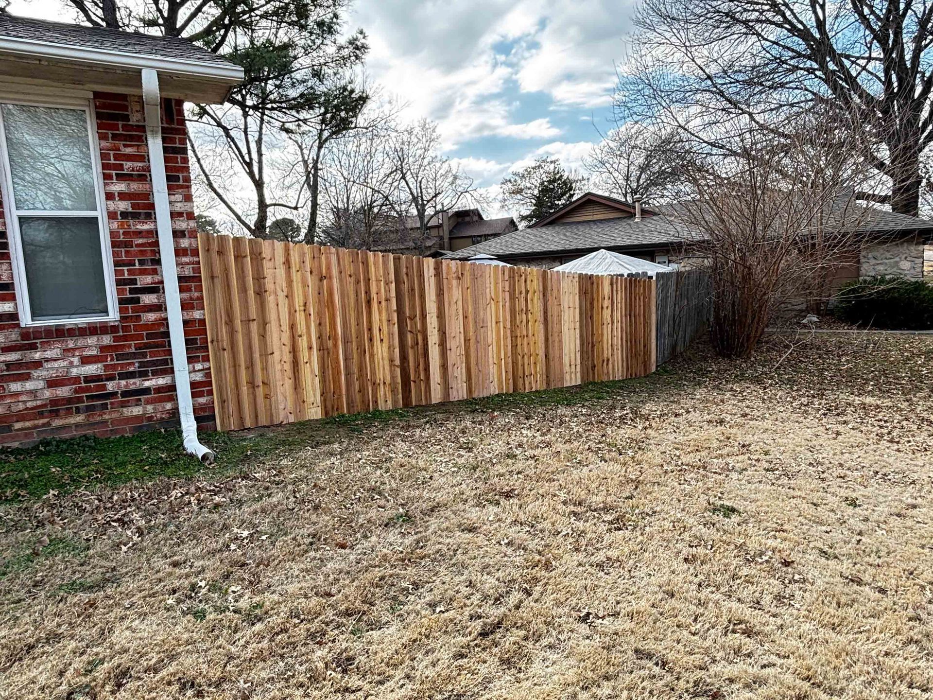 Backyard with a wooden privacy fence beside a red brick house and leafless trees