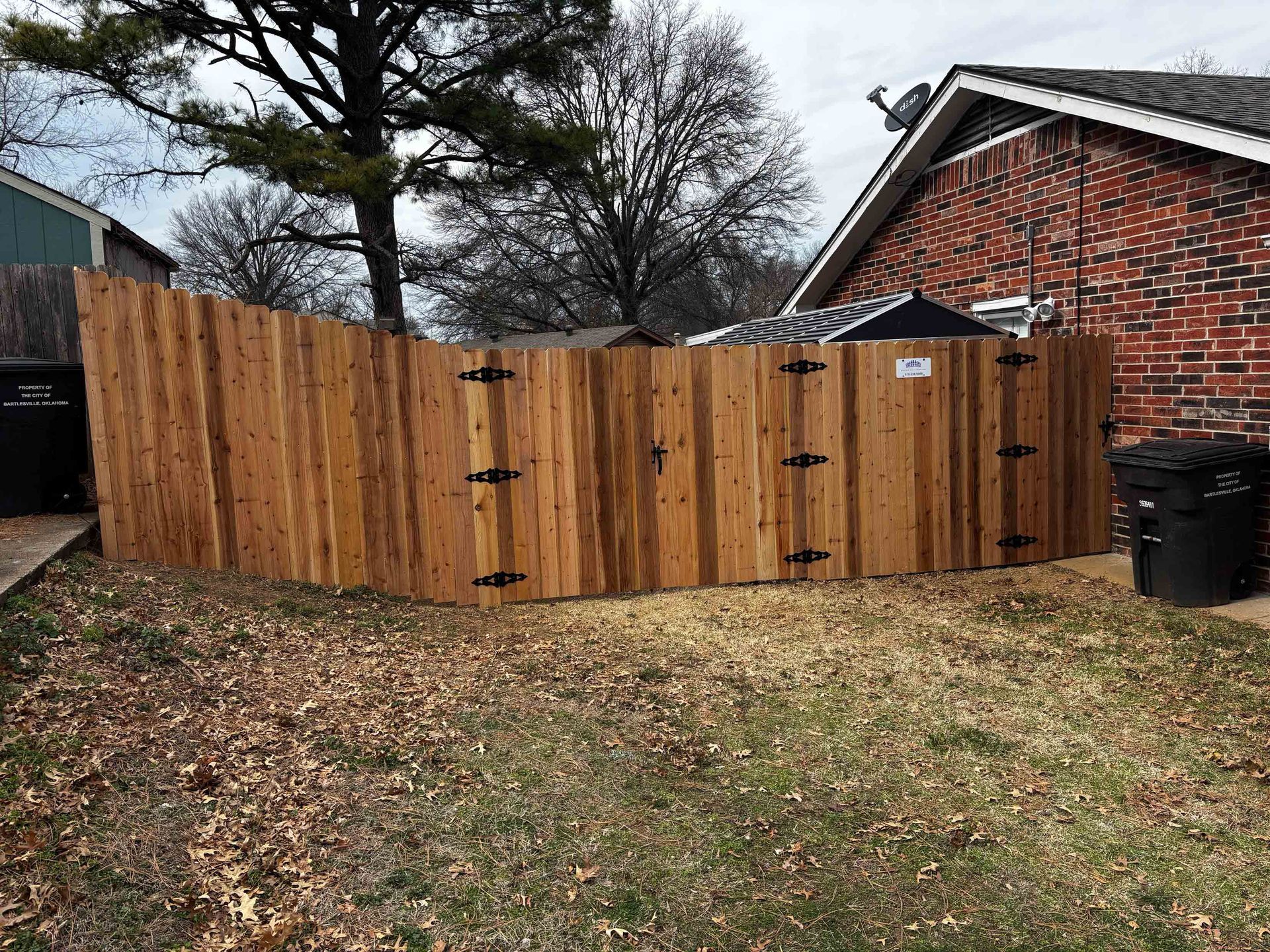 Wooden privacy fence in a backyard beside a brick house and leaf-covered lawn