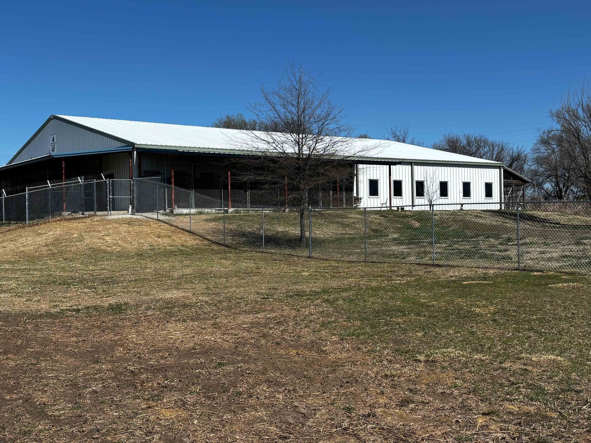 Single-story white building with a covered porch on a grassy hill under a clear blue sky