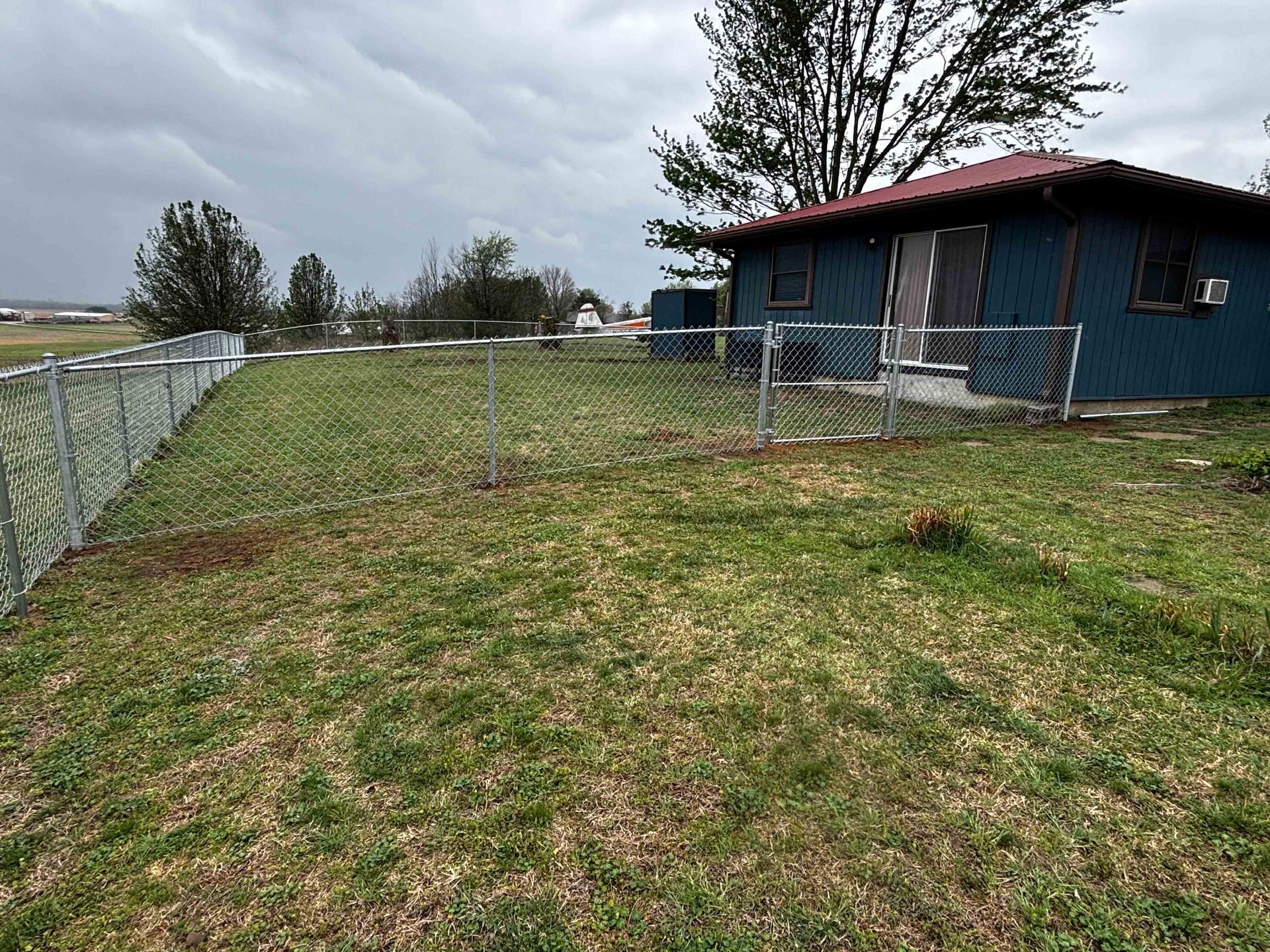 Grassy fenced yard beside a blue building under a cloudy sky