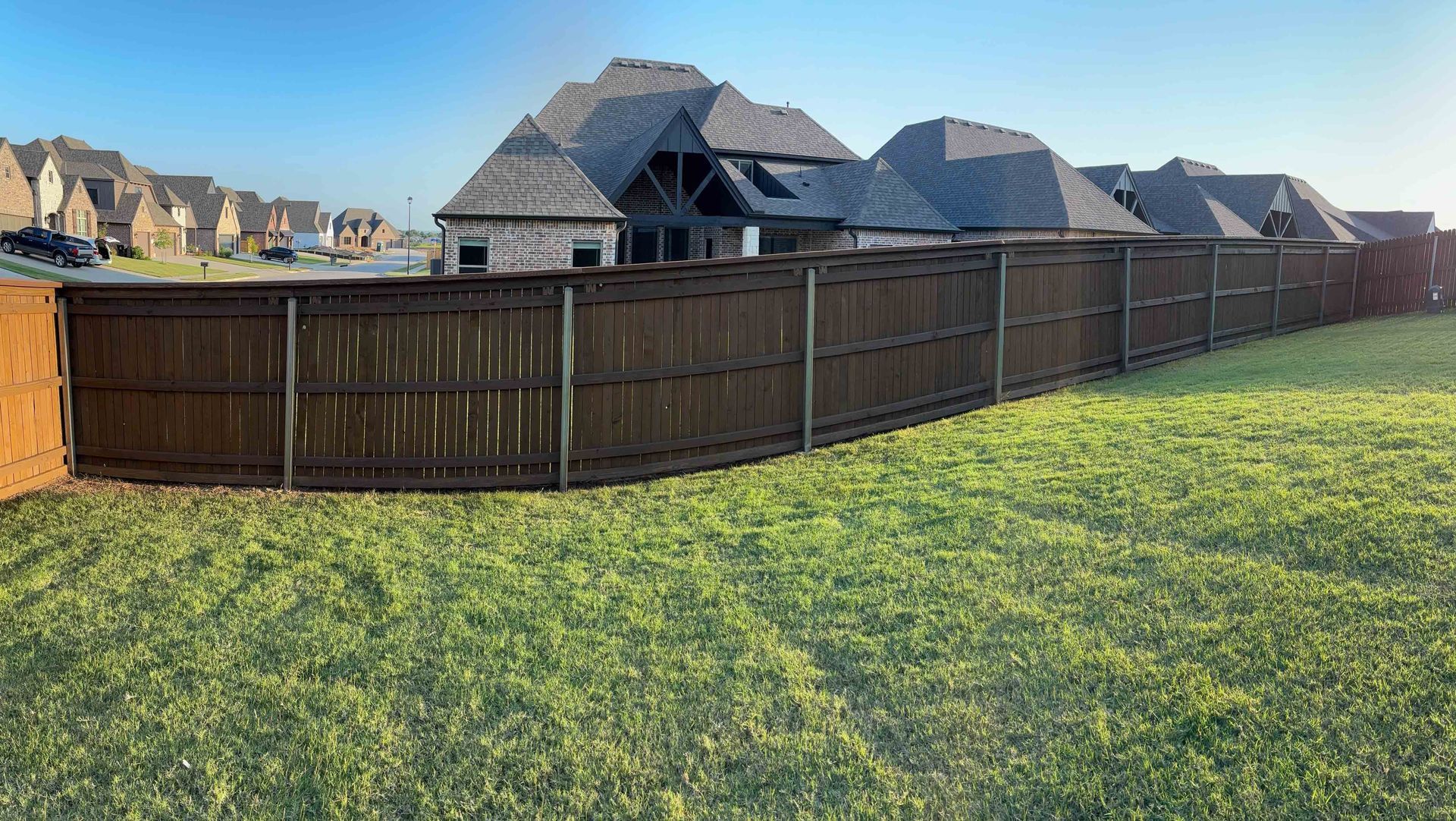 Wooden fence bordering a grassy field with thatched-roof buildings in the background under a clear sky