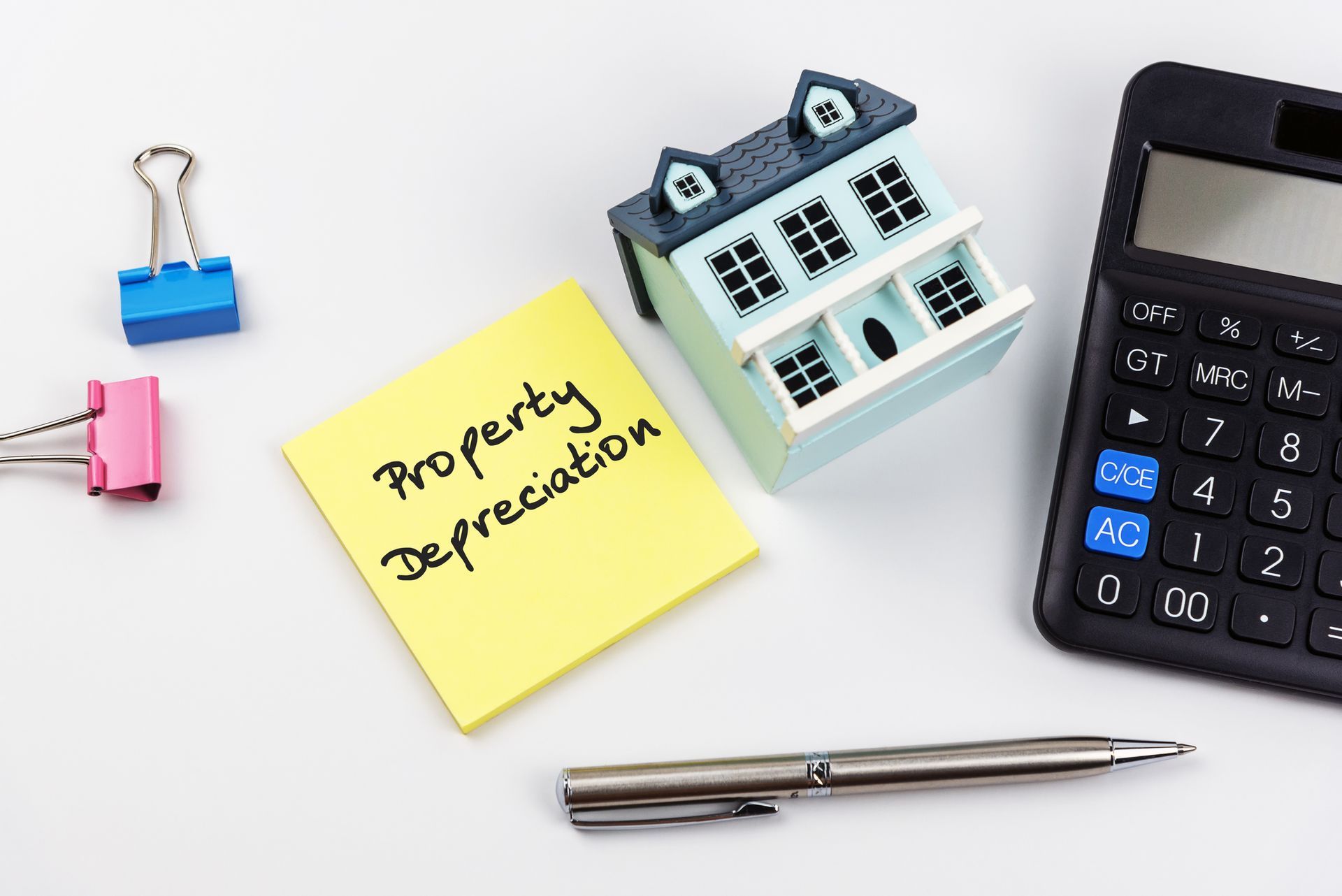 Investment Property Depreciation concept on sticky note with calculator, pen and clips.