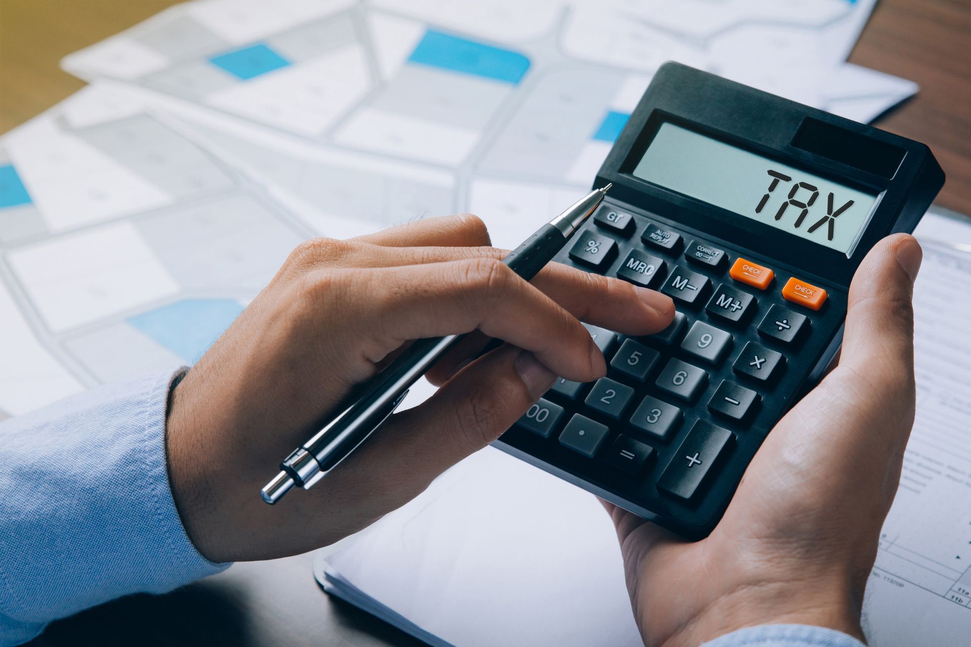 A man holding a pen & a calculator with “tax“ on the screen & documents of land purchases.